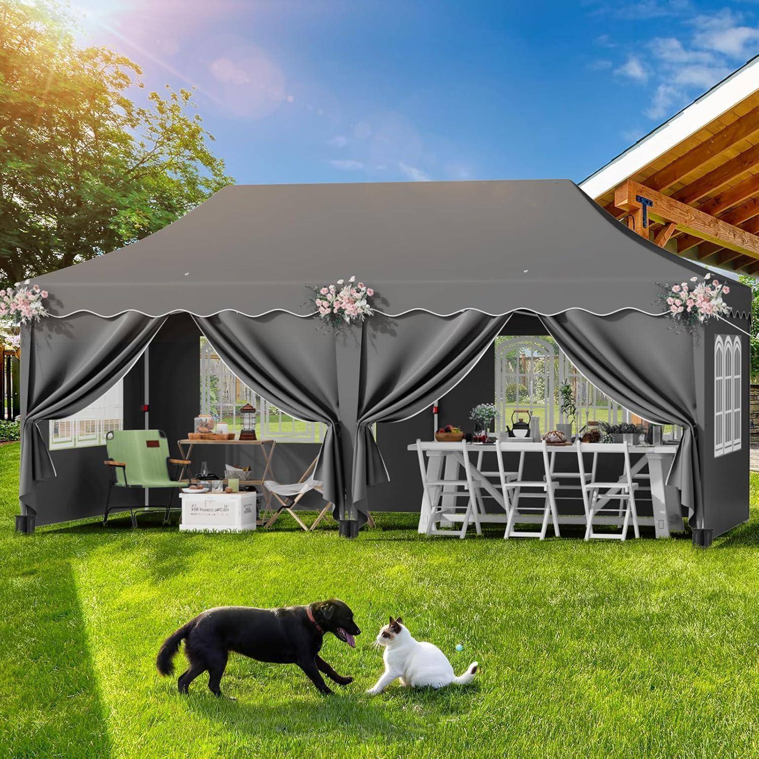 Graues Außenevent-Zelt auf einem Rasen mit weißen Stühlen, Tischen und Blumendekorationen; ein schwarzer Hund und eine weiße Katze spielen davor.