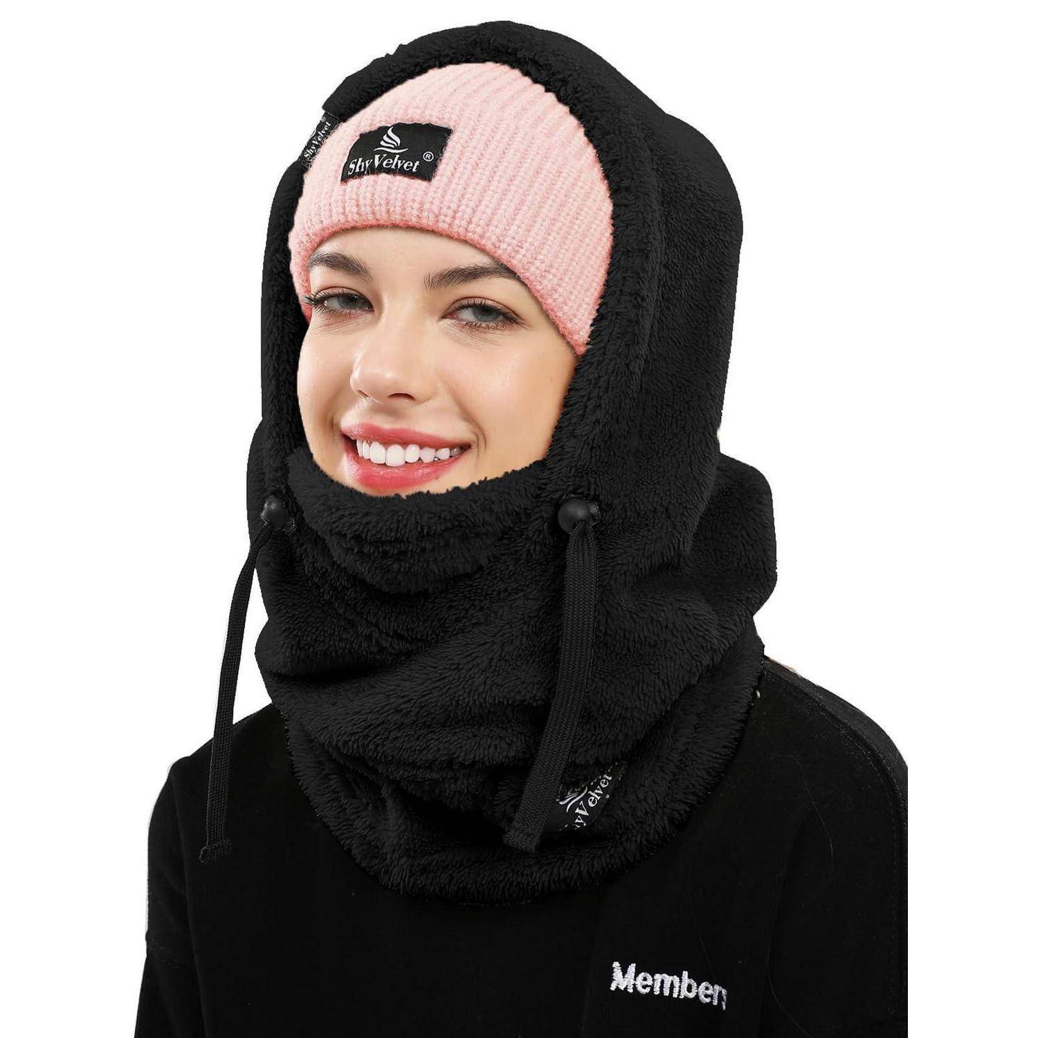 Frau, die von den Schultern aufwärts vor weißem Hintergrund gezeigt wird, trägt eine schwarze Fleece-Sturmhaube und eine rosa Beanie.