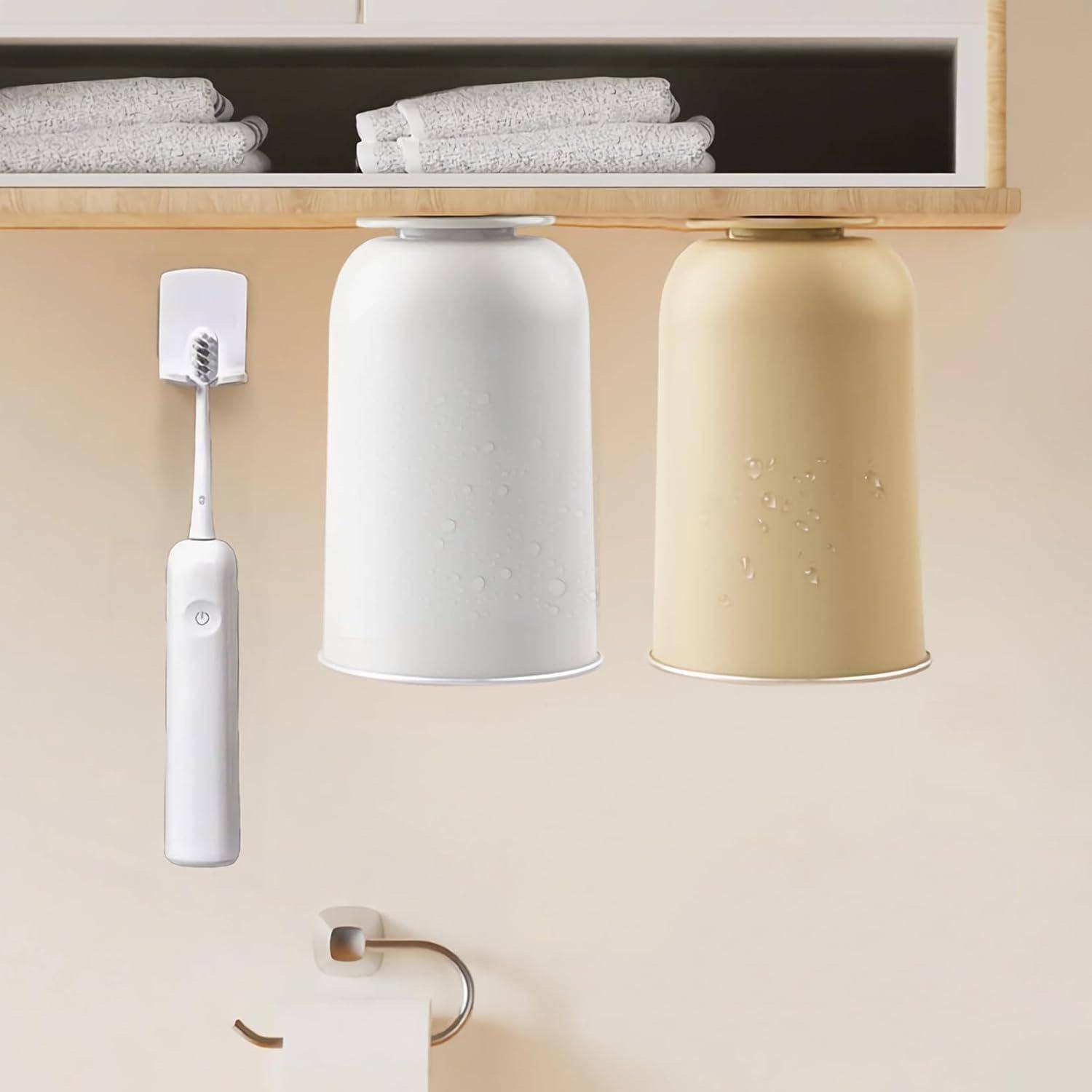 Weiße elektrische Zahnbürste neben zwei umgekehrt angebrachten Bechern, einer weiß und einer beige, hängend unter einem Regal mit gefalteten Handtüchern.
