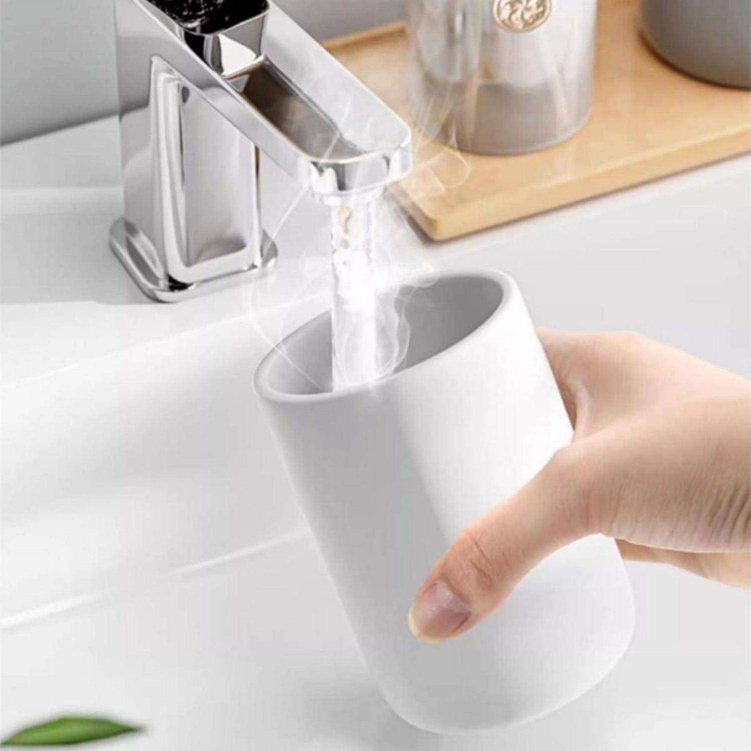 Eine weiße Tasse unter einem modernen Chromhahn an einem Waschbecken von Hand spülen.