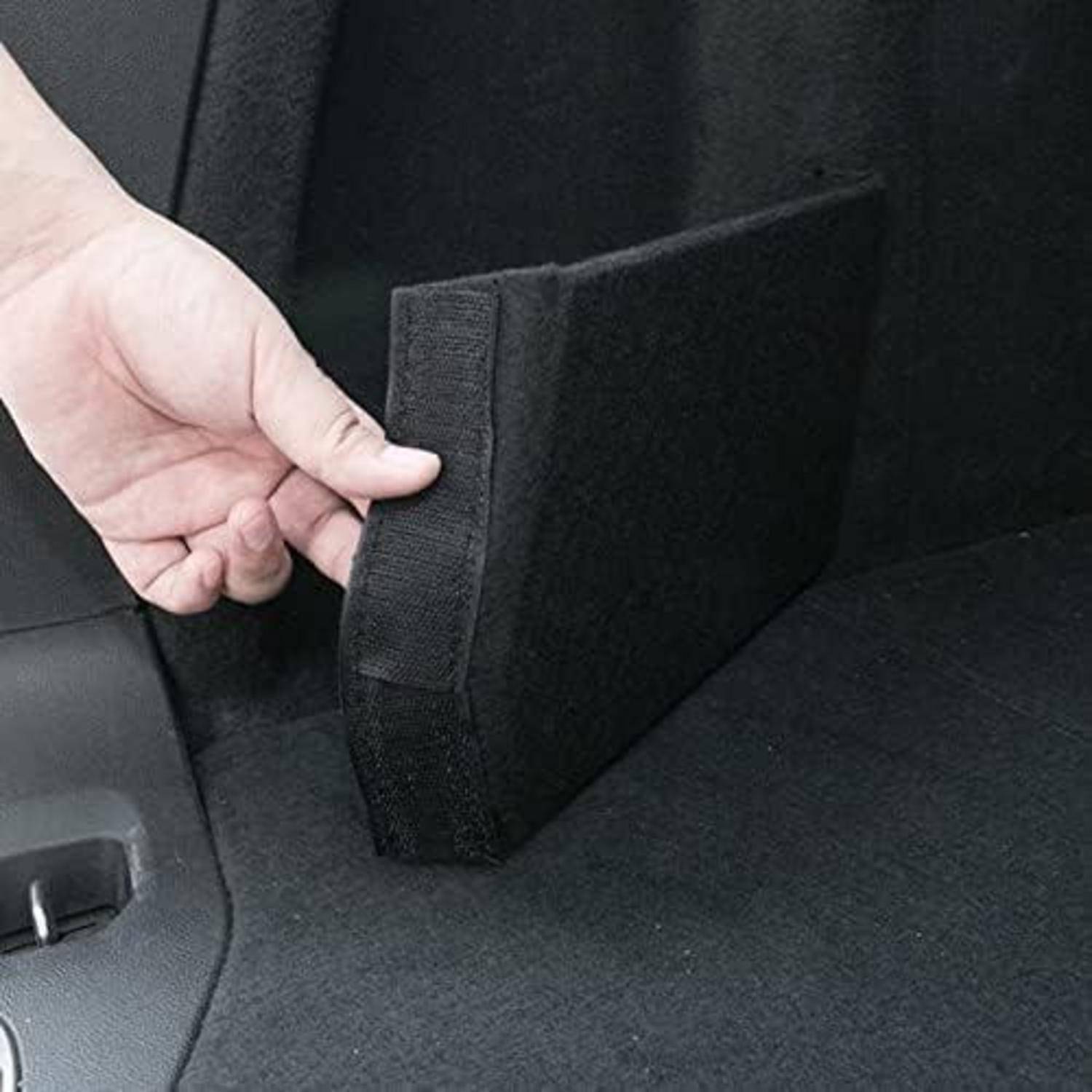 Hand hält einen schwarzen, mit Klettverschluss versehenen Schaumstoff-Trennsteg in einem Autokofferraum oder Ladebereich und zeigt eine abnehmbare Lagerkammer.