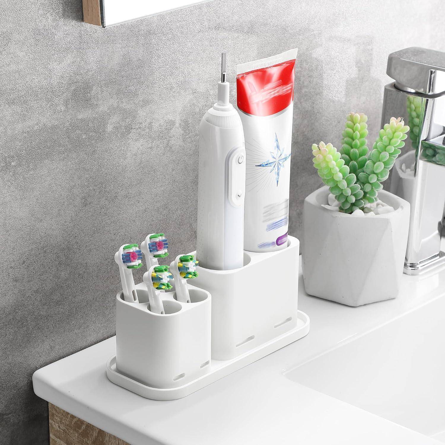 Badezimmer-Arbeitsplatte-Organizer, der eine elektrische Zahnbürste, vier manuelle Zahnbürsten, Zahnpasta und eine kleine Pflanze neben einem Spülbecken-Wasserhahn hält.