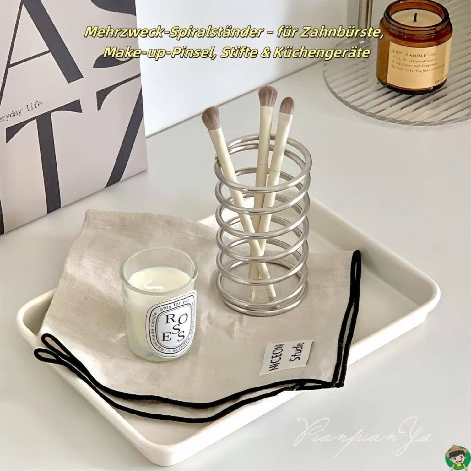 Metallische Spiralhalter für Zahnbürsten, Schminkpinsel und Küchengeräte, angezeigt auf einem Tablett mit einer kleinen Kerze und einem Tuch.