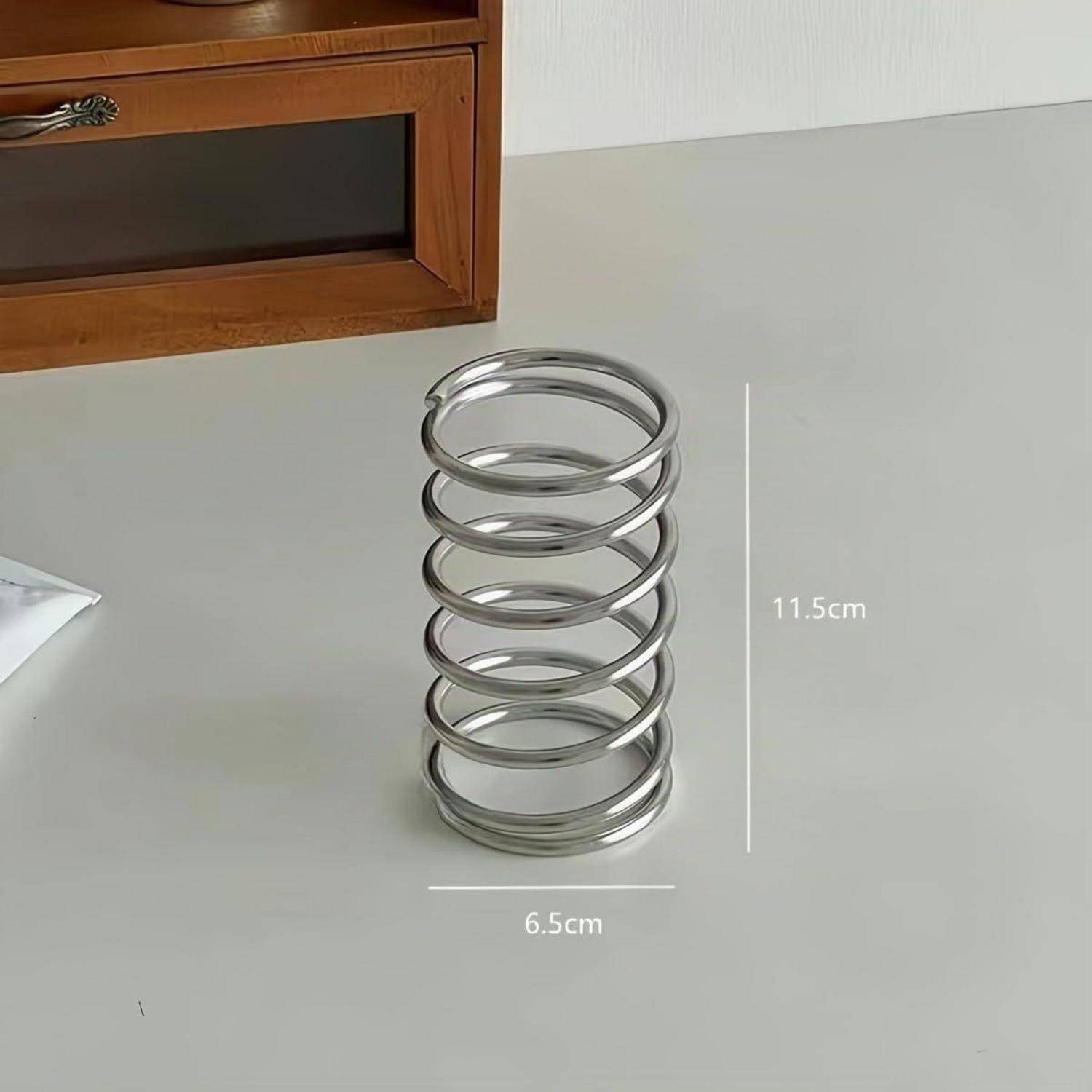 Eine Metallwendelfeder auf einem Tisch, beschriftet mit 11,5 cm Höhe und 6,5 cm Breite.