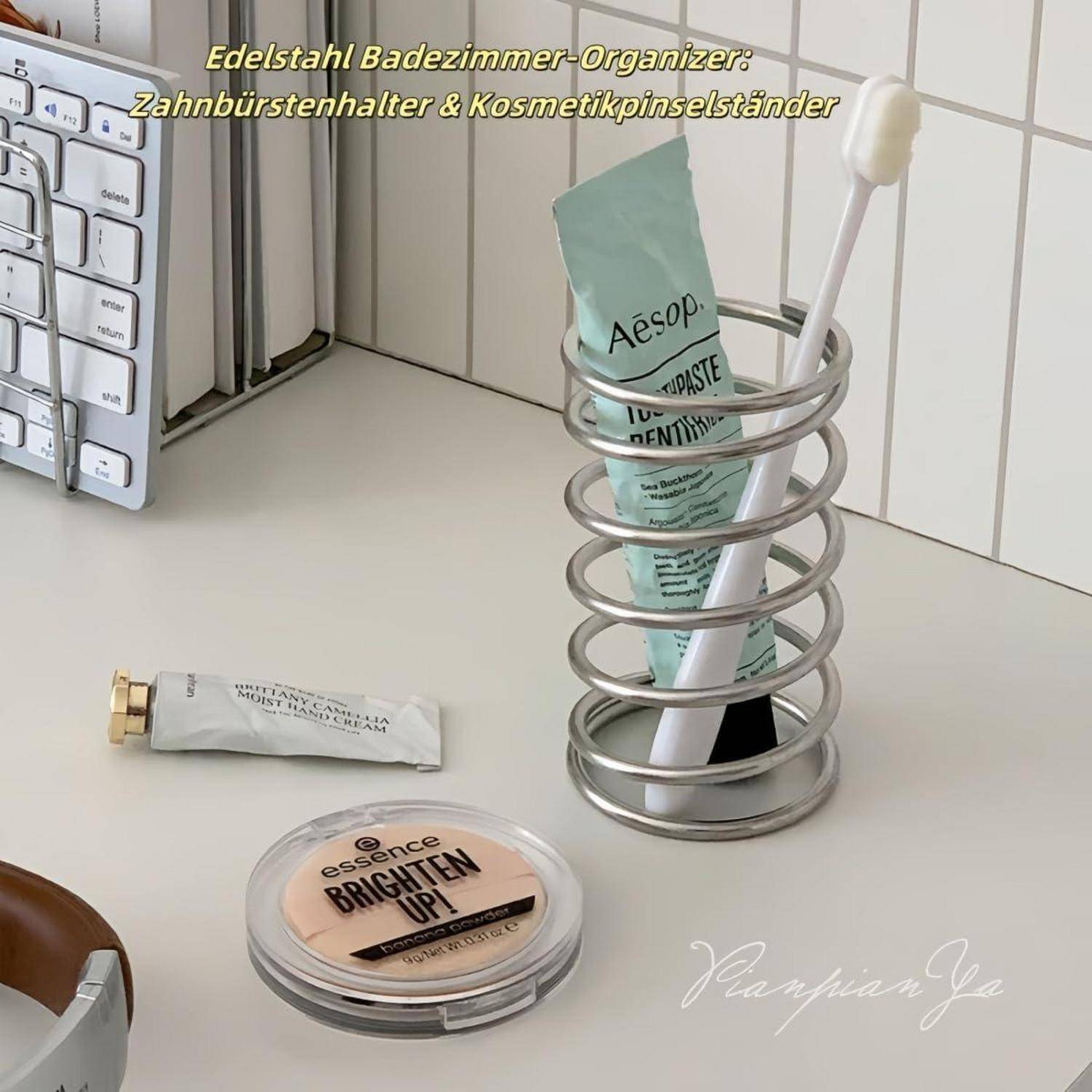 Badezimmerorganizer mit spiralförmigem Metallhalter, der eine Zahnpastatube und eine Zahnbürste neben Kosmetika auf einer Frisierkommode lagert, auf Deutsch als „Edelstahl-Badezimmerorganizer