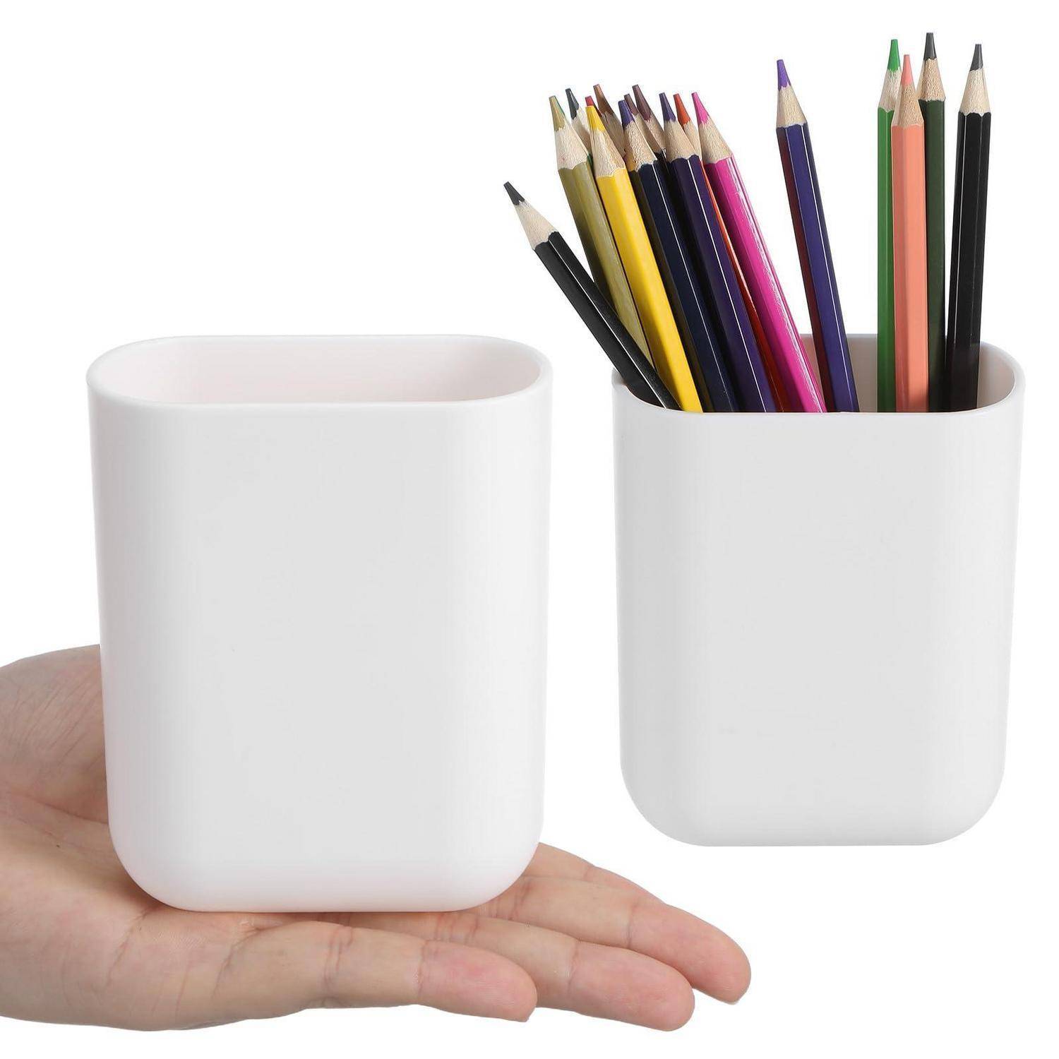 Hand, die eine weiße Tasse neben einem passenden weißen Stifthalter hält, der mit Buntstiften gefüllt ist und die Größe und Form des Halters zeigt.