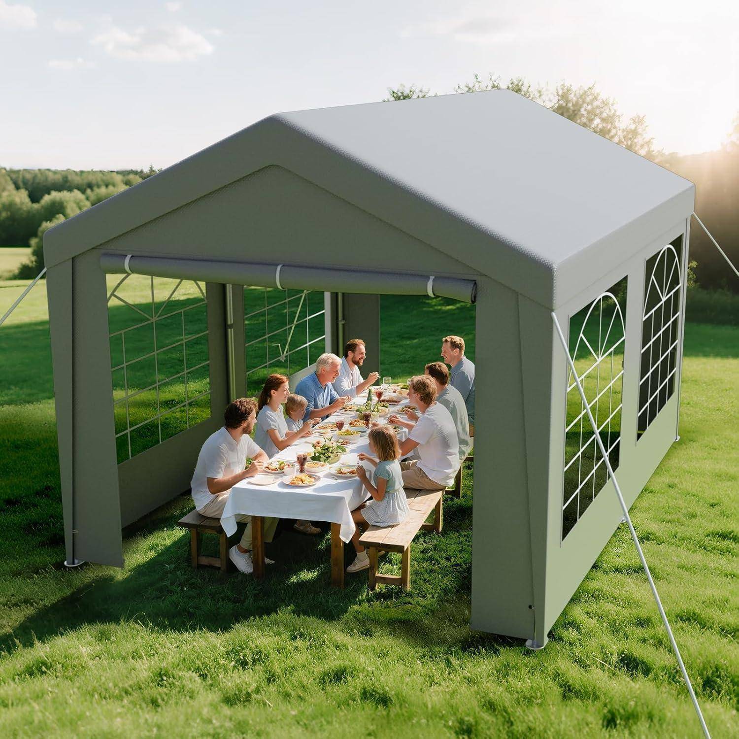 Eine Familie sitzt an einem langen Tisch in einem großen grauen Außenpavillonzelt und nimmt eine Mahlzeit auf einem Rasenplatz in der Sonne zu sich.
