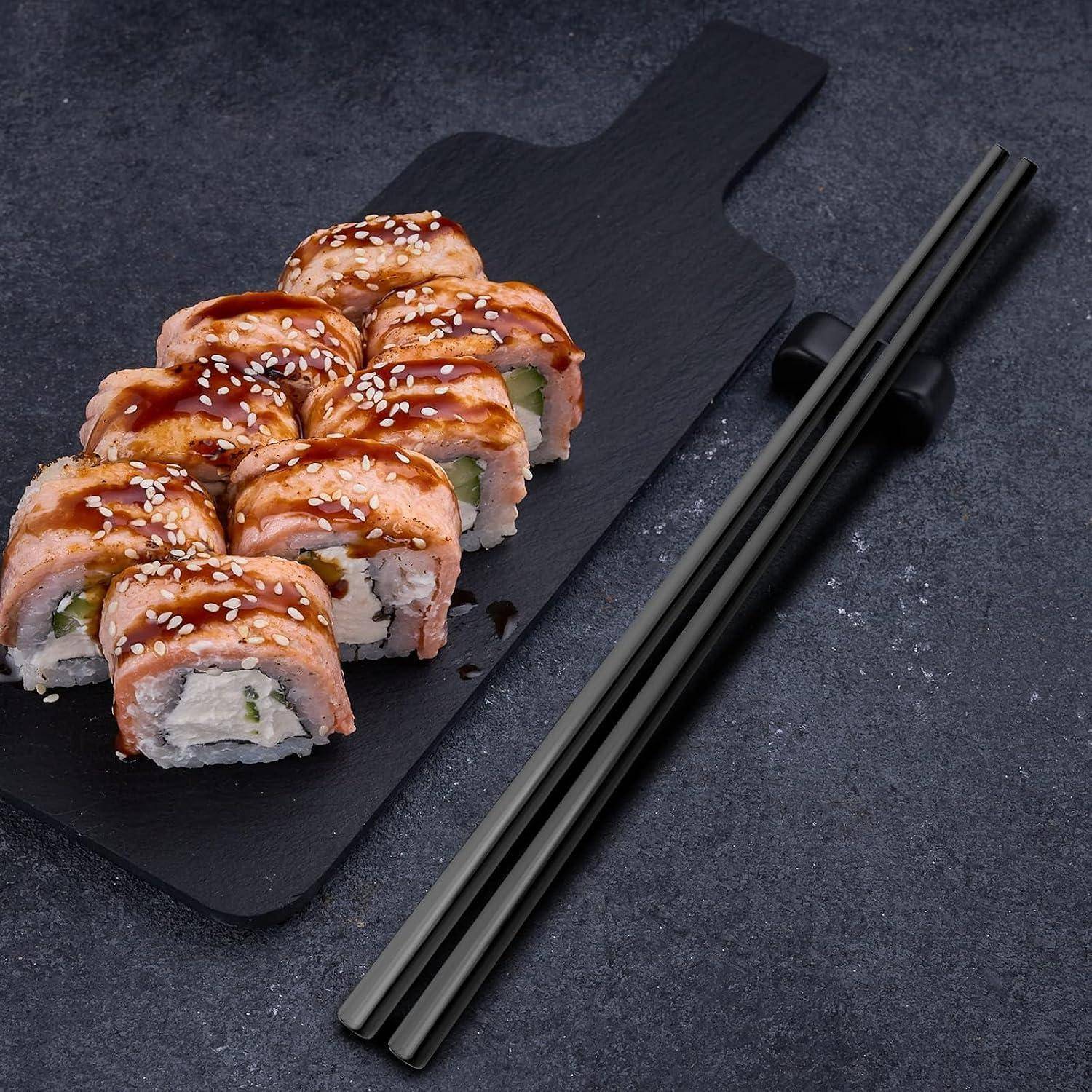 Sushi-Rollen mit gebratenem Lachs und Sesamkörnern auf einem schwarzen Servierbrett, daneben Essstäbchen.