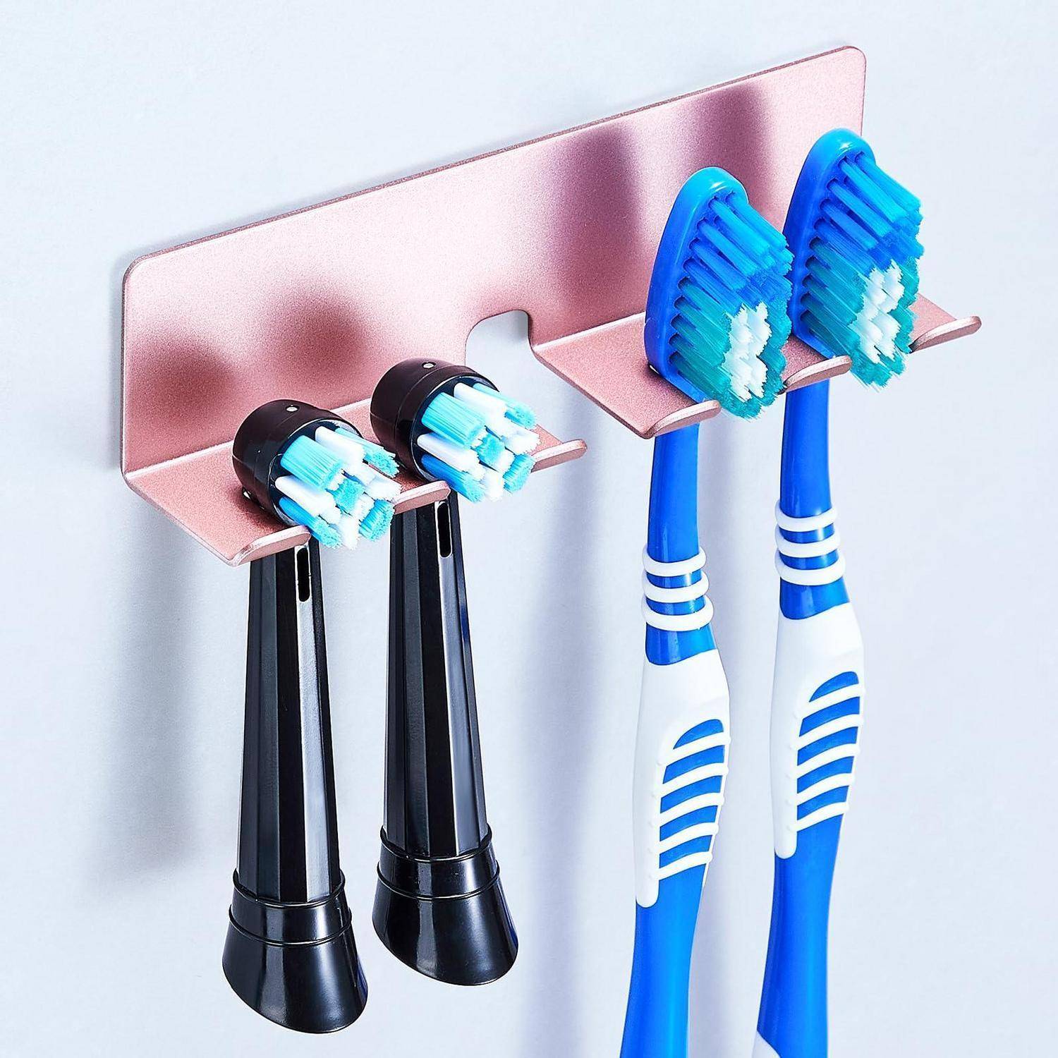 An der Wand montierter Zahnbürsenhalter zur Aufbewahrung von vier elektrischen Zahnbürsten mit zwei schwarzen und zwei blauen Griffen auf einer rosa Rückwand.