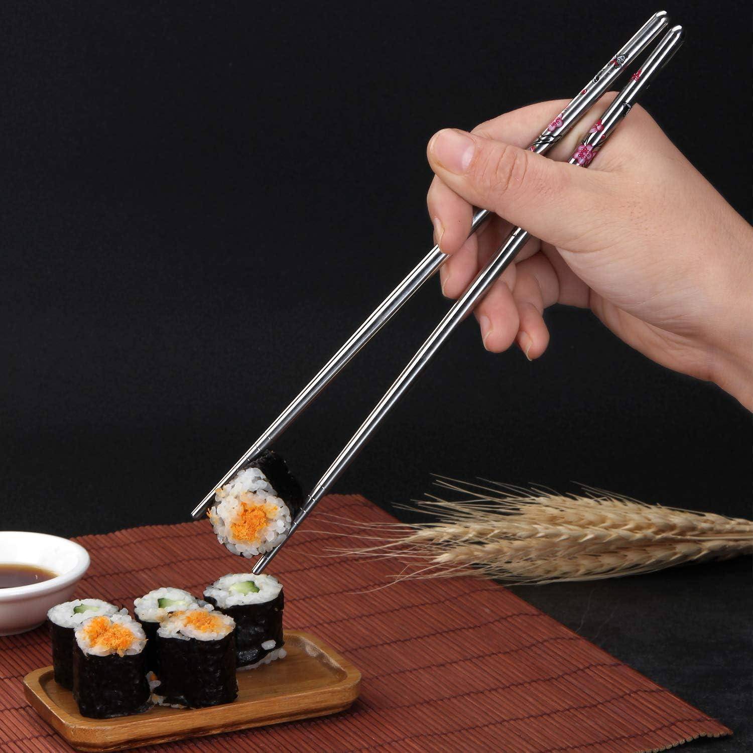 Hand, die mit Stäbchen Sushi-Rollen von einem kleinen Holzteller nimmt, mit Dipping-Soße, Bambussmatte und Weizenhalmen auf dunklem Hintergrund.