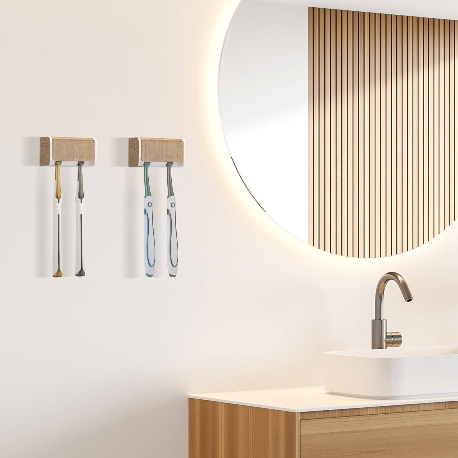 Modernes Badezimmer mit zwei wandmontierten Zahnburtstenhaltern, einem runden beleuchteten Spiegel und einem Waschbecken auf einem Holzwaschtisch.