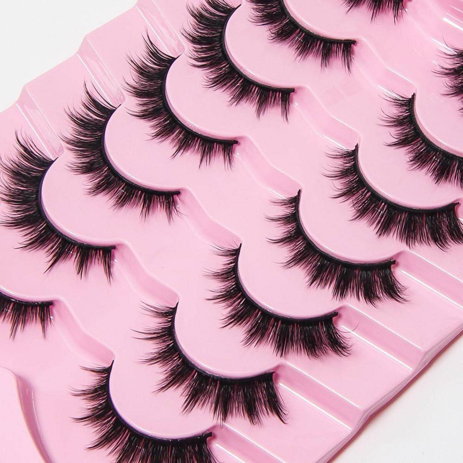 Sortierte künstliche Wimpern in rosa Verpackung, in Reihen auf weißem Hintergrund angeordnet.