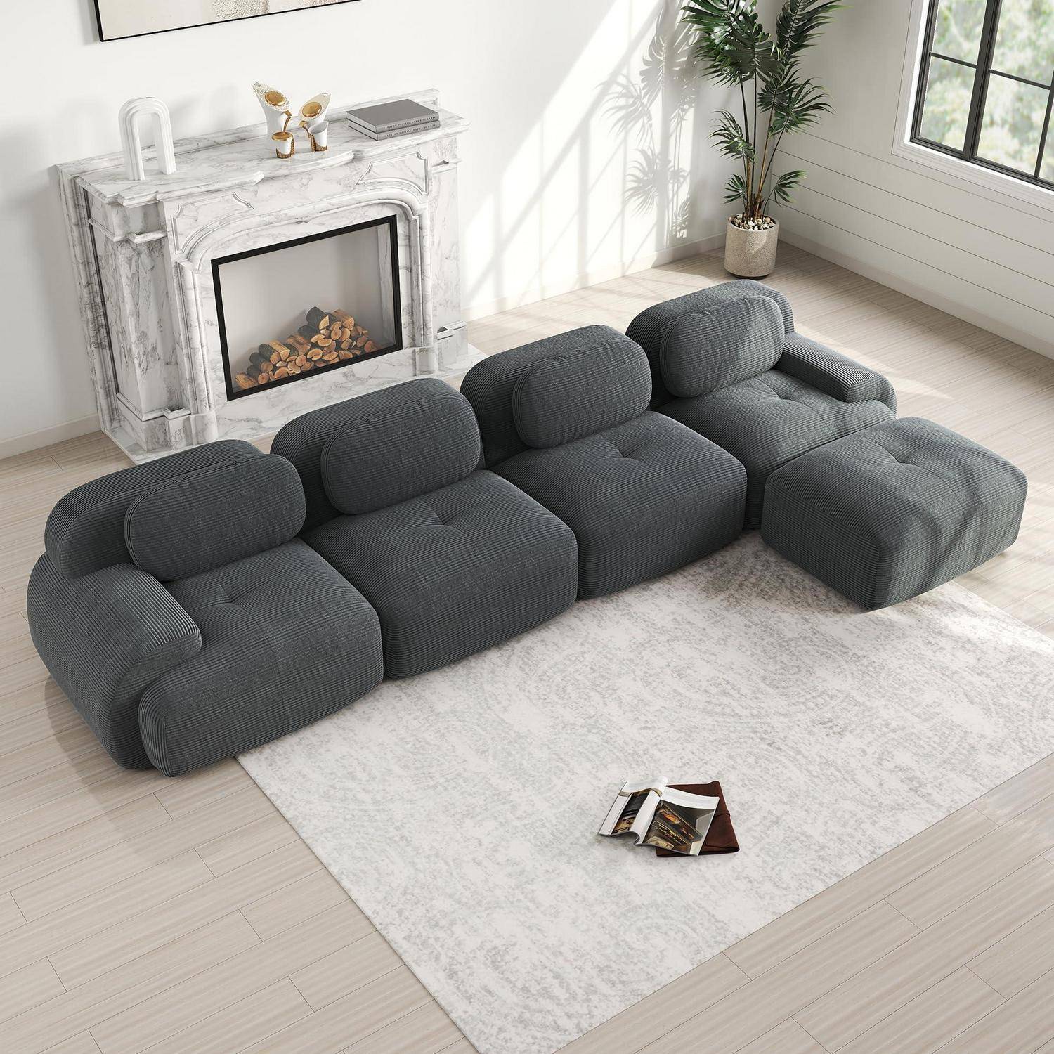 Dunkelgraues modulares Ecksofa mit weichen gerundeten Kissen in einem hellen Wohnzimmer, angeordnet um einen weißen Teppich neben einem Marmorkamin.