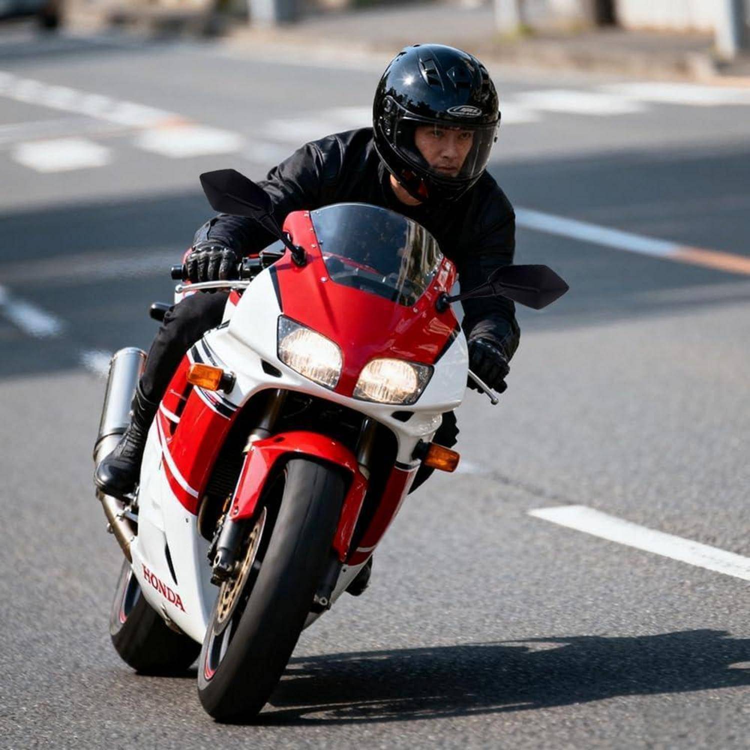 Motorradfahrer in schwarzer Ausrüstung, der sich in eine Kurve auf einem rot-weißen Sportmotorrad auf einer Straße neigt.
