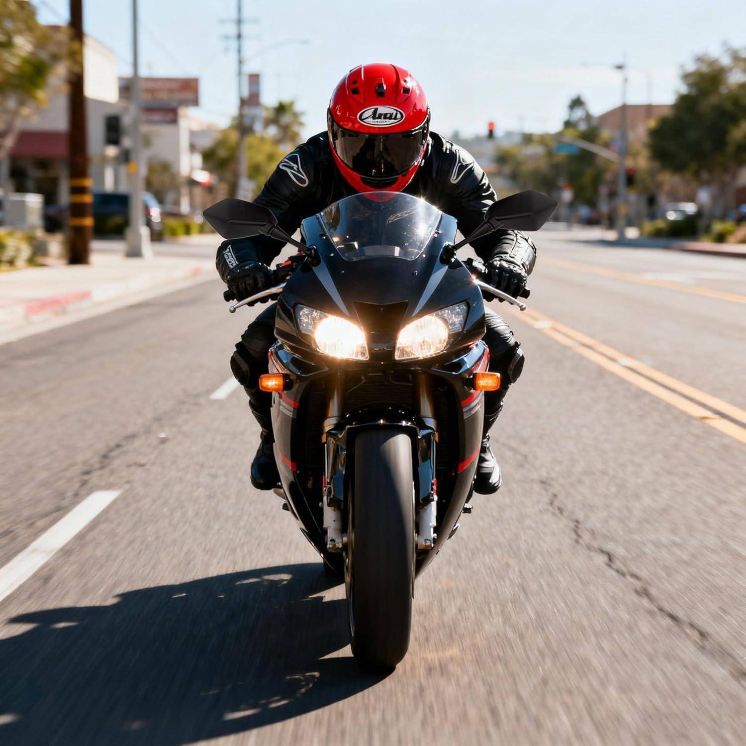 Motorradfahrer mit rotem Helm auf einem schwarzen Sportmotorrad, der auf einer sonnigen Stadtstraße auf die Kamera zufährt.