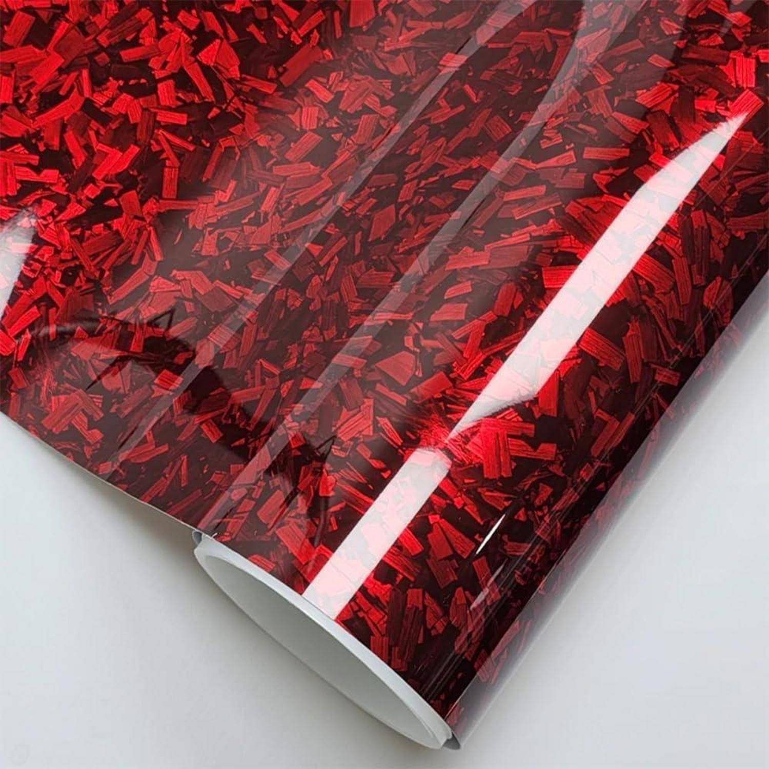 Nahaufnahme von glänzendem roten gemustertem Geschenkpapier, das zu einem Zylinder gerollt auf einer weißen Oberfläche liegt.