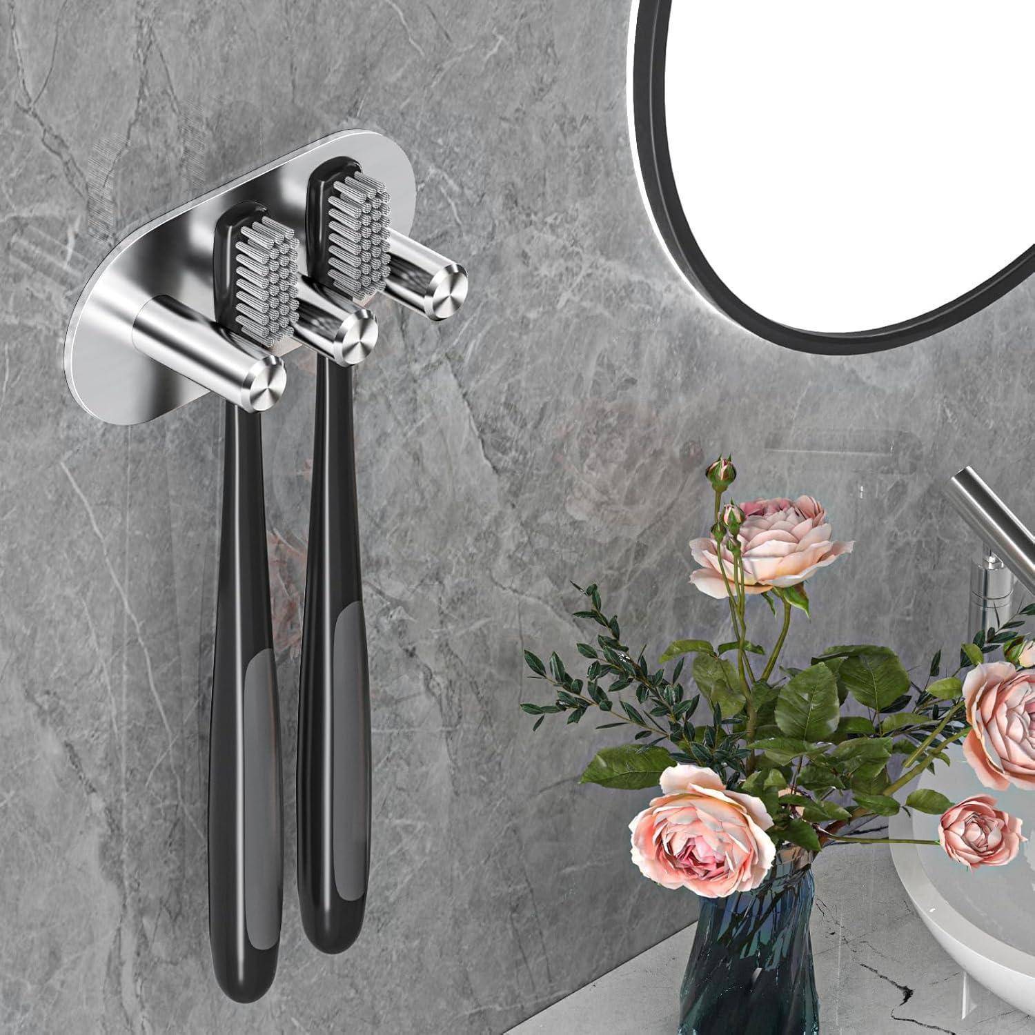 Moderner wandmontierter Zahnbürstenhalter mit zwei schwarzen Zahnbürsten, neben einem Spiegel und einer Vase mit rosa Blumen auf einer grauen Steinwand.