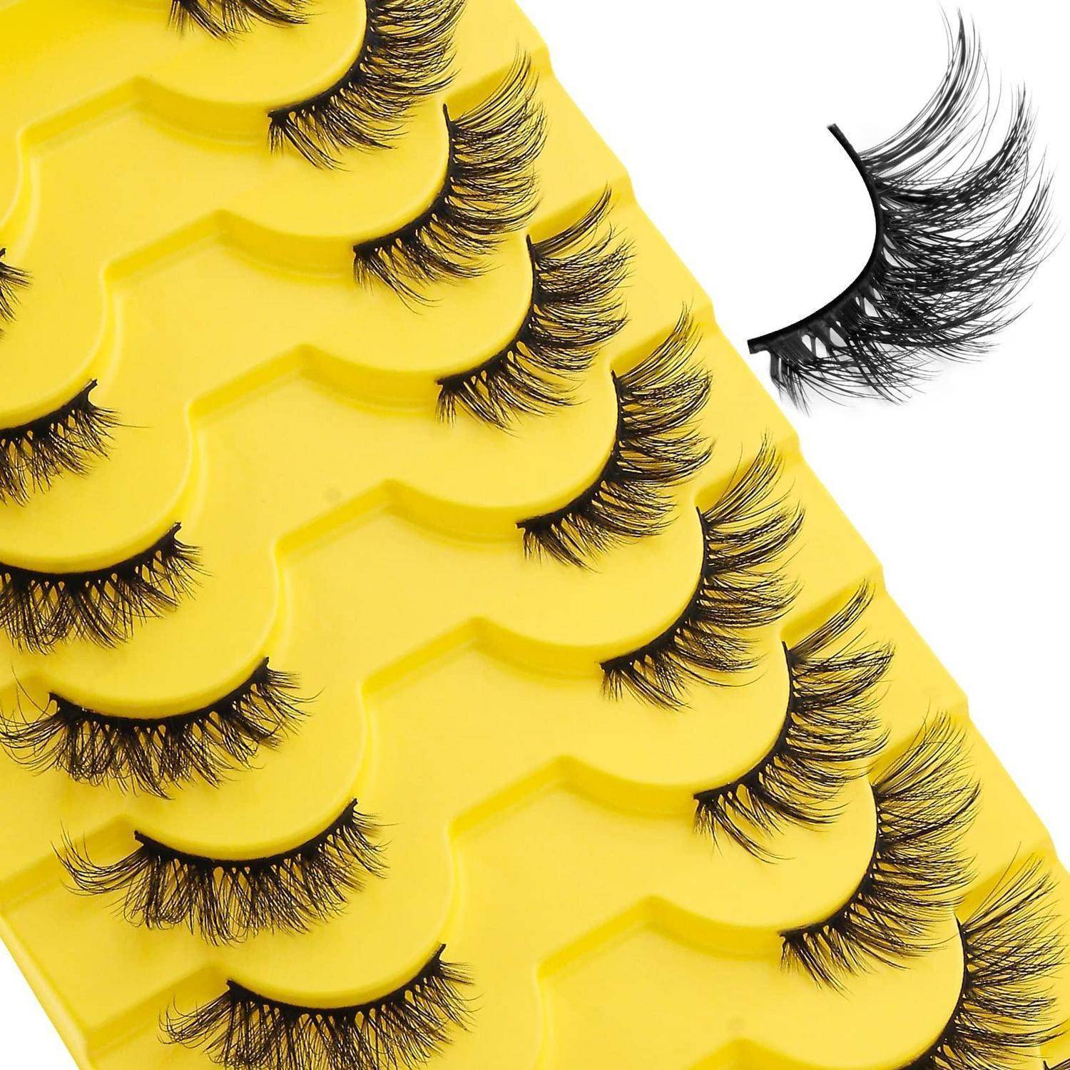 Nahaufnahme mehrerer falscher Wimpern, die auf gelben Tabletts angeordnet sind, mit einer losen Wimpernhaarverlängerung auf der rechten Seite auf weißem Hintergrund.