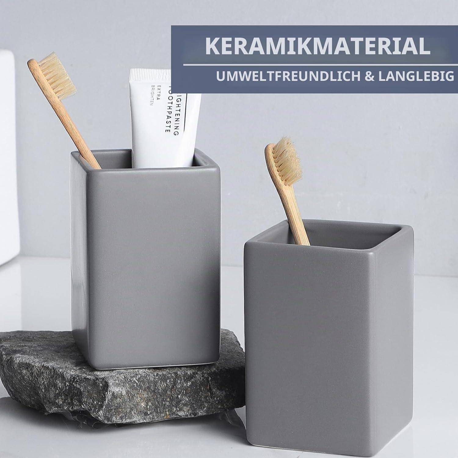 Zwei graue keramische Badezimmerhalter auf einer Arbeitsplatte, einer mit einer Zahnbürste und Zahnpasta, mit deutschem Text, der „KERAMIKMATERIAL