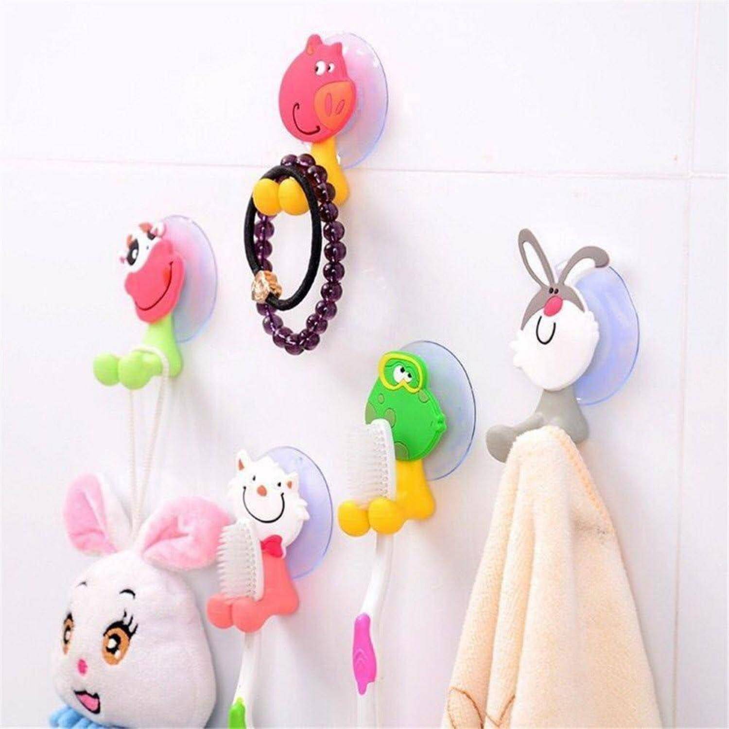 Bunte tierförmige Wandhaken halten ein Armband, eine Bürste und ein Handtuch an einer weißen gefliesten Wand.