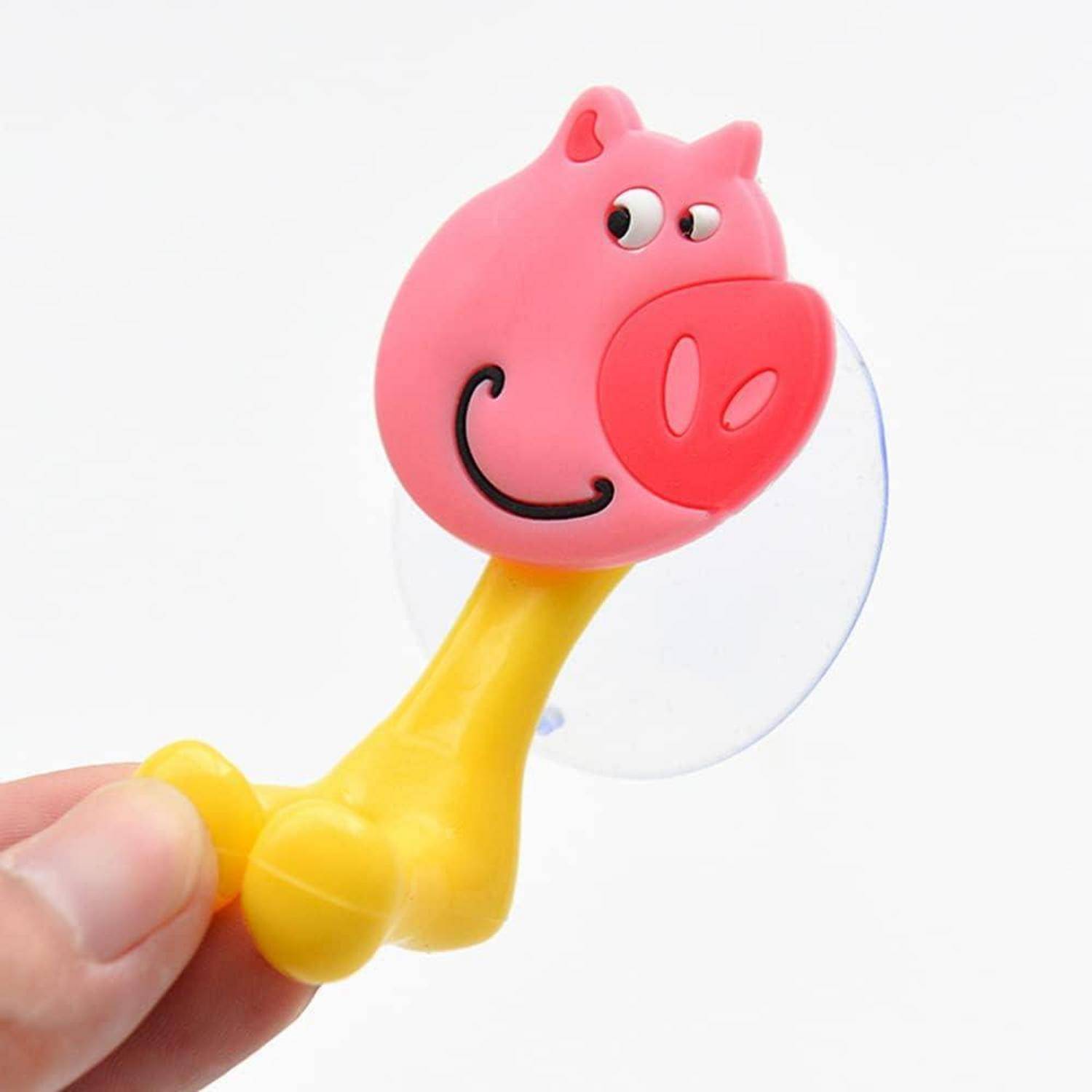 Nahaufnahme eines rosa, schweineförmigen Saugnapf-Spielzeugs mit gelbem Griff, das von einer Hand gegen einen weißen Hintergrund gehalten wird.