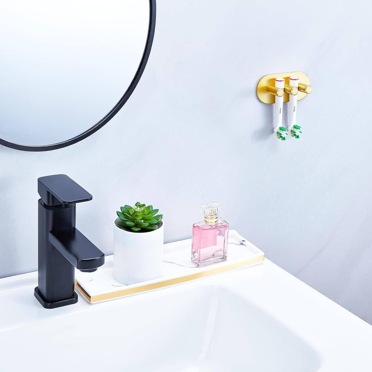 Modernes Badezimmerbecken mit schwarzem Wasserhahn, rundem Spiegelrahmen, weitem Tablett mit einer kleinen Sukkulente und einer rosa Parfümflasche sowie einem an der Wand montierten Zahnbürstenhalter.