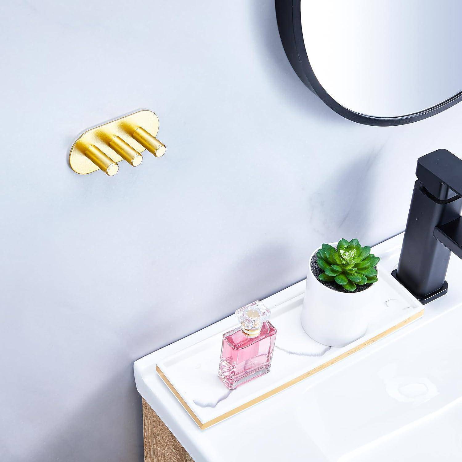 Modernes Badezimmermöbel mit weißer Arbeitsplatte, goldener Wandarmatur, rundem Spiegel, schwarzem Wasserhahn, kleiner Pflanze und rosa Parfümflasche.