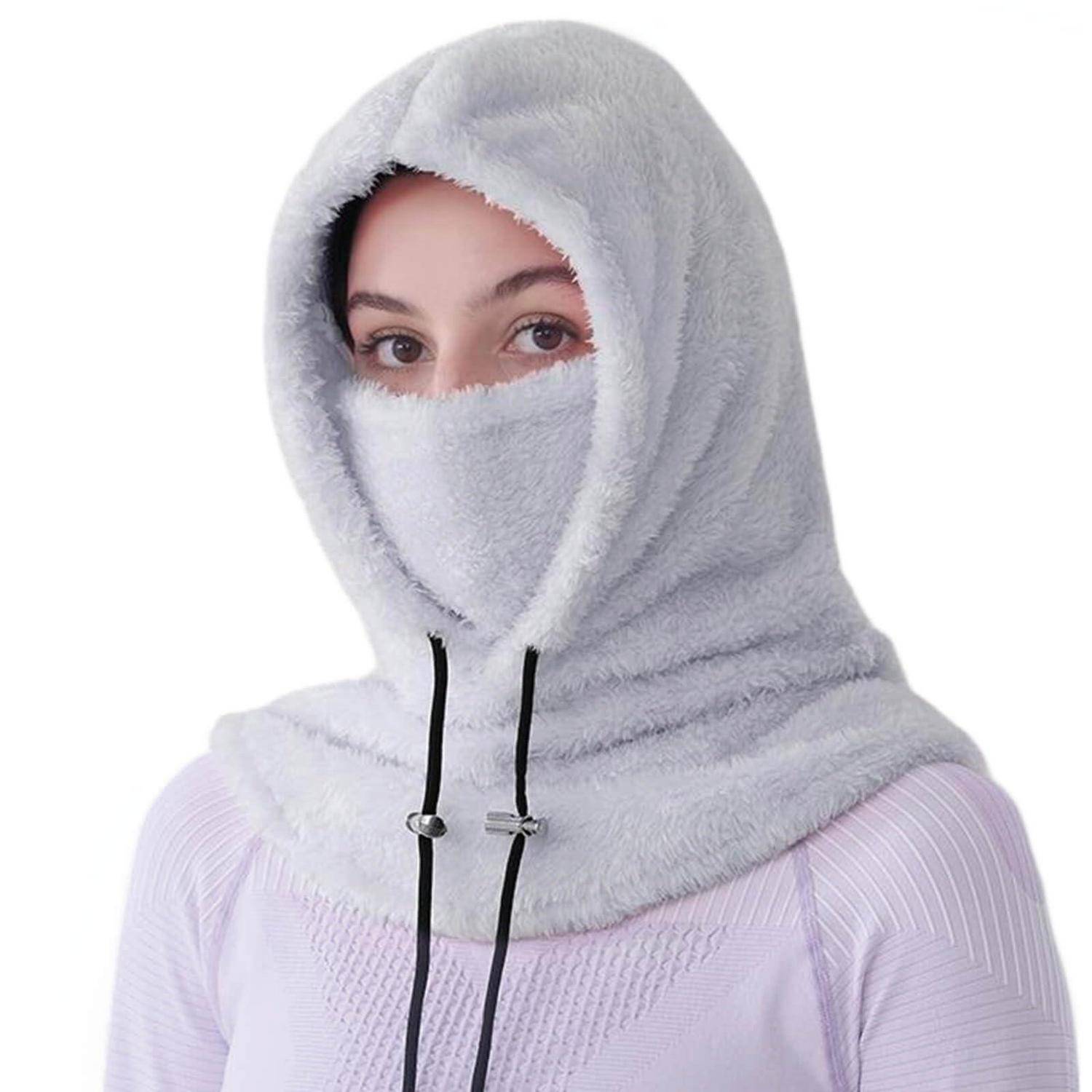 Person, der eine flauschige hellgraue Kapuze und Gesichtsbedeckung trägt, mit nur sichtbaren Augen, vor einem einfachen weißen Hintergrund.