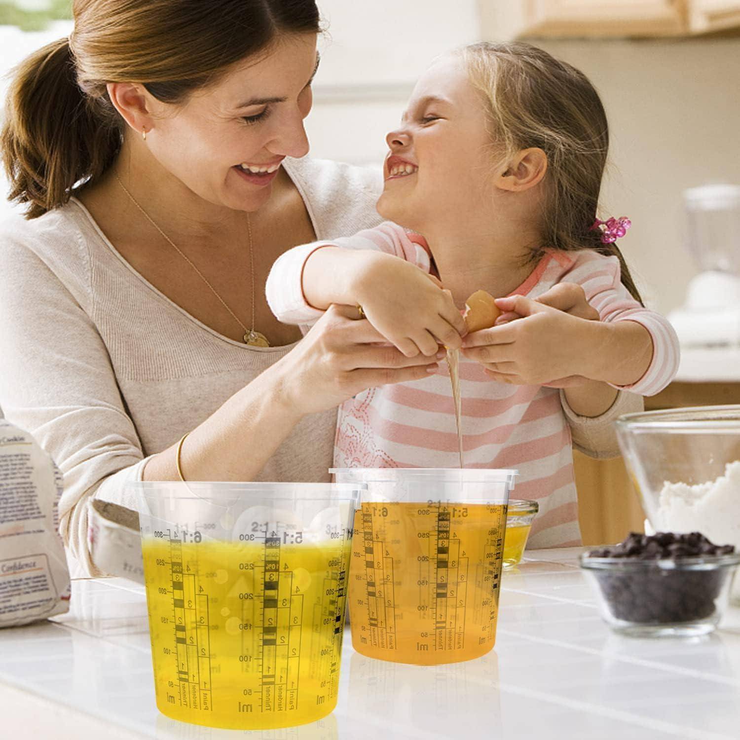 Mutter und kleine Tochter backen zusammen in einer Küche, lächeln, während sie Zutaten in durchsichtigen Messbechern abmessen.