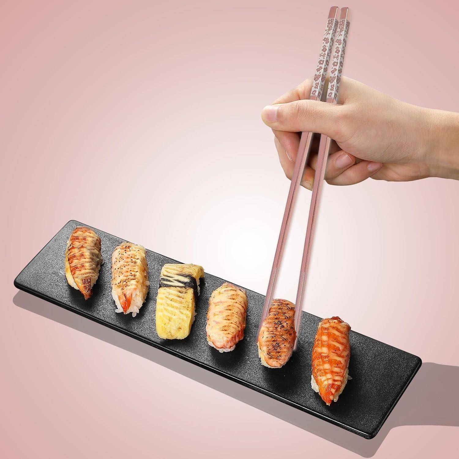 Hand, die mit Stäbchen ein Stück Sushi-Mix auf einem schwarzen Tablett aufnimmt.