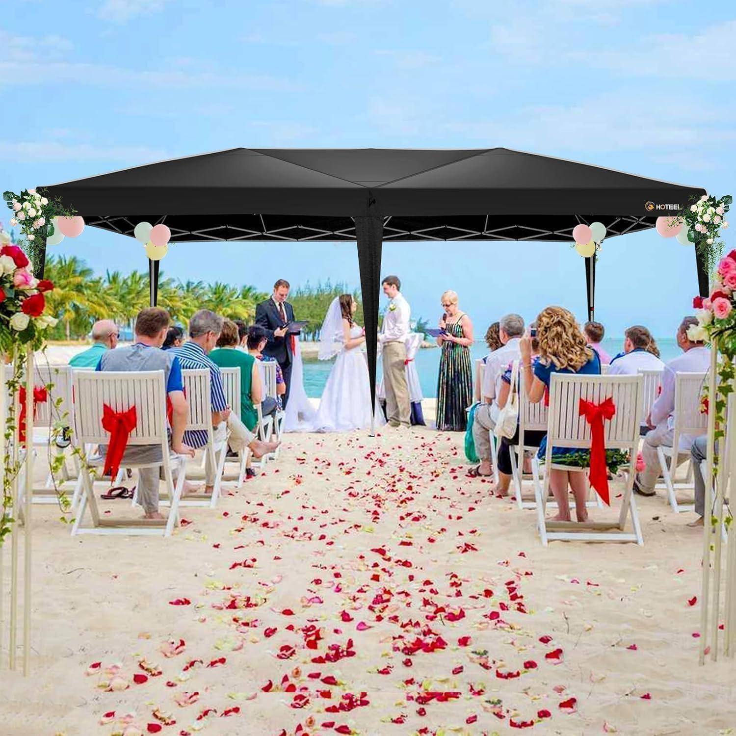 Strandtrauung unter einem schwarzen Baldachin, mit Braut und Bräutigam am Altar, sitzende Gäste auf beiden Seiten und Rosenblätter, die den Sand bedecken.