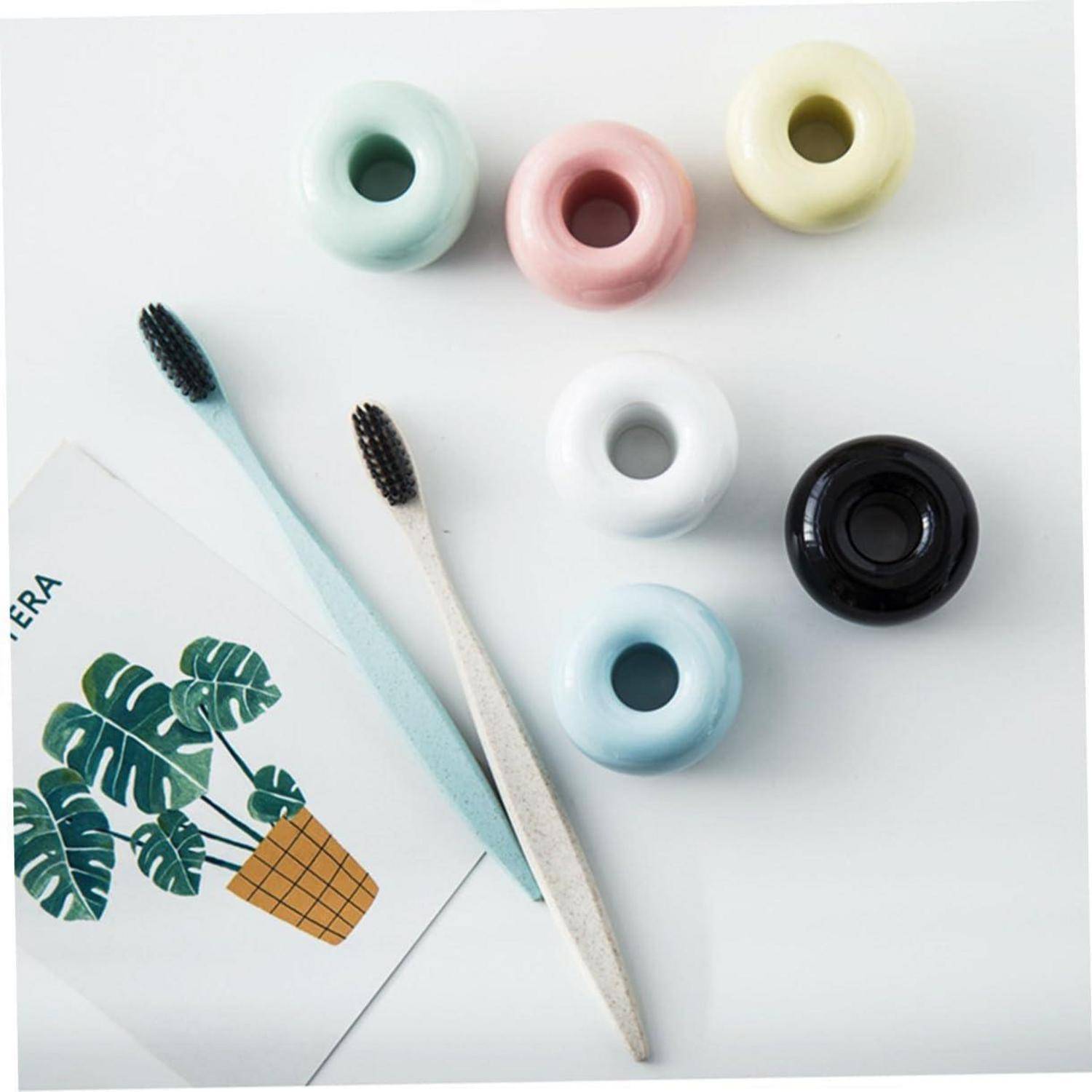 Verschiedene pastellfarbene und schwarze Behälter für Make-up oder Mascara mit zwei Mascara-Bürsten und einer Karte mit Blattmotiv auf einer weißen Oberfläche.