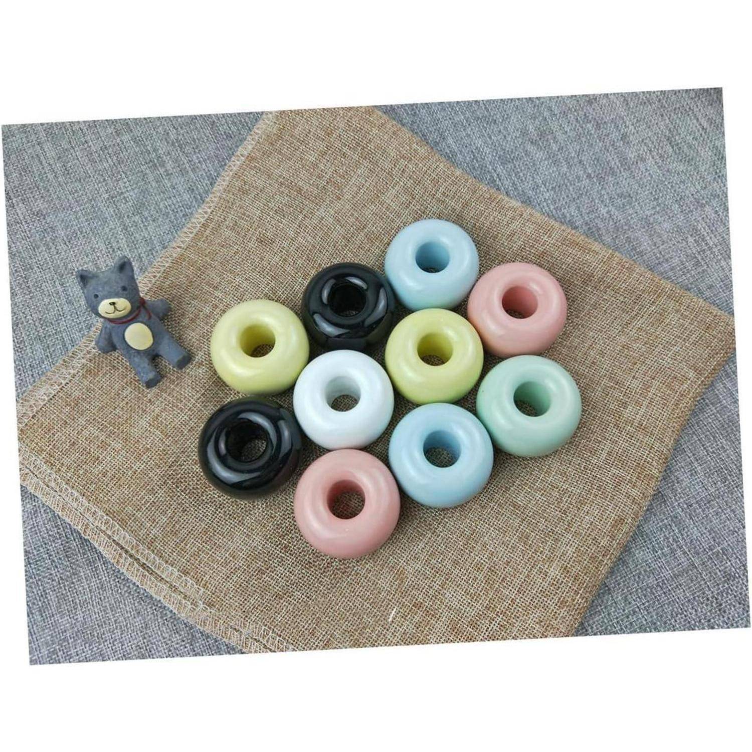 Kleiner grauer Teddybär neben einem Stapel von pastellfarbenen ringförmigen Donuts auf einer Jutematte über grauem Stoff.