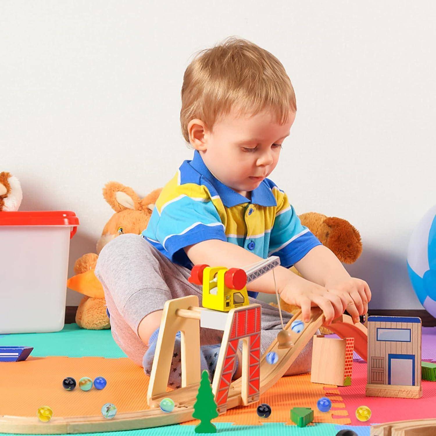Kleinkind spielt mit Holzbauklötzen und einem kleinen Kransatz auf einer bunten Spielmatte, umgeben von Kuscheltieren.