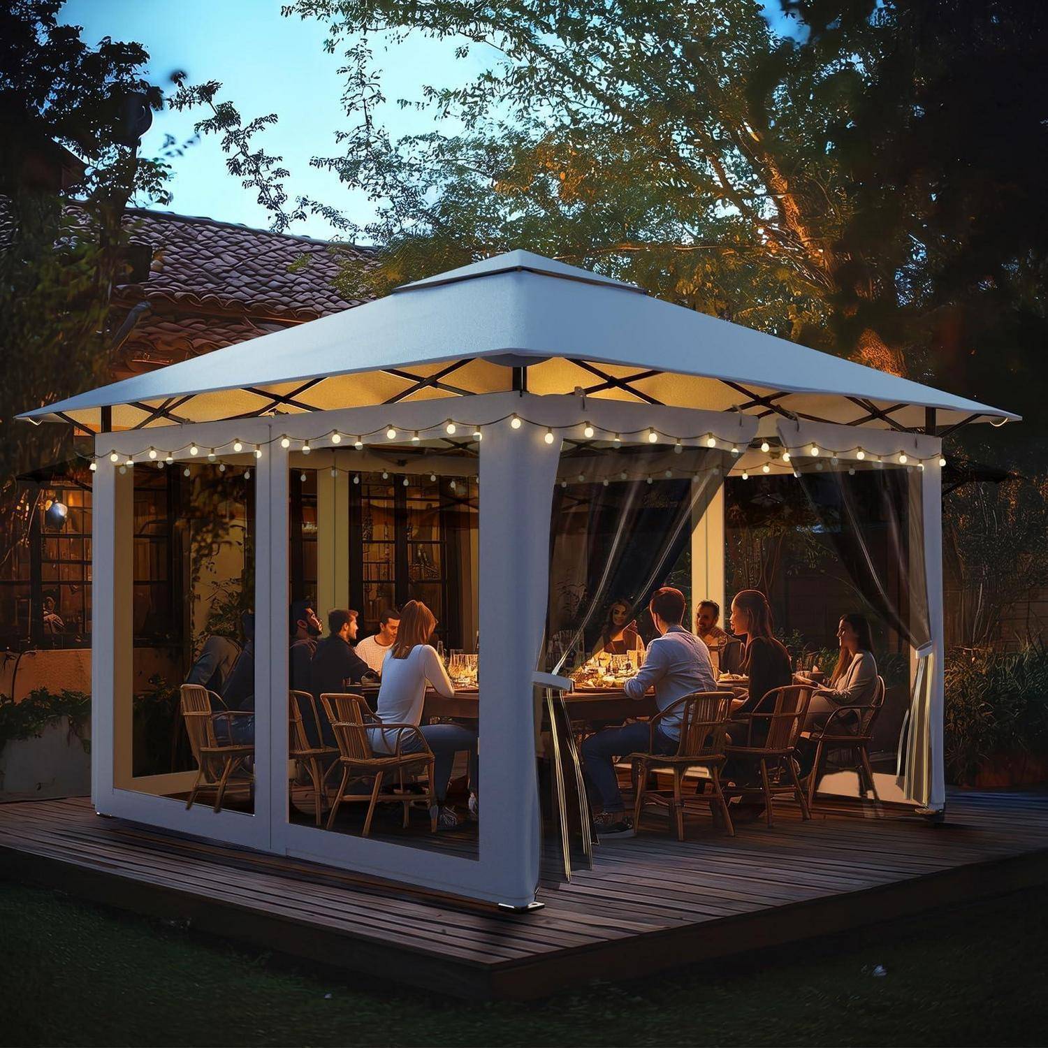 Menschen, die bei Einbruch der Dämmerung zusammen in einer beleuchteten Gartenlaube mit Lichterketten und Vorhängen auf einer Holzterrasse speisen.