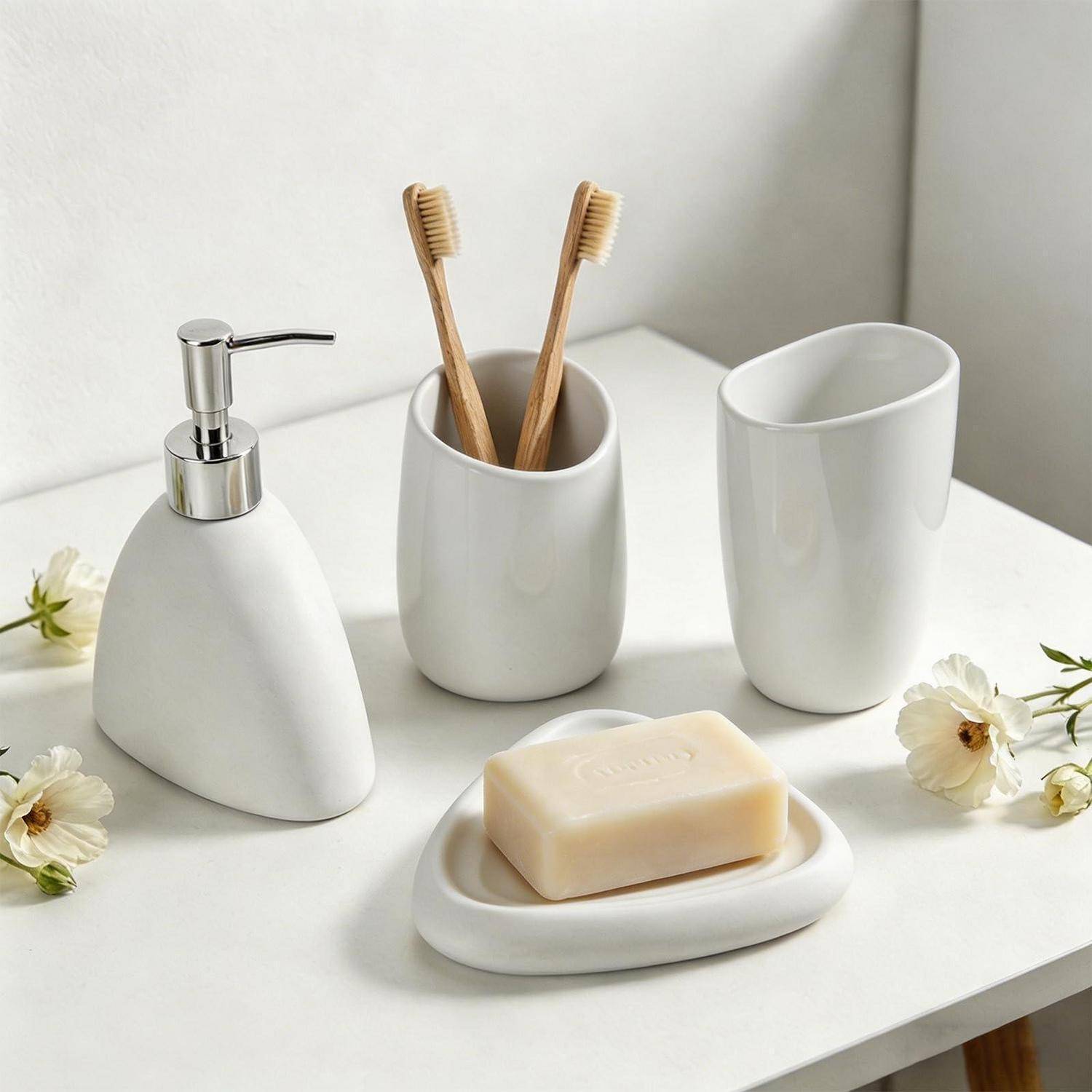 Minimales weißes Badezimmerset mit Seifenspender, Zahnbürstenhalter, Becher und Seifenschale auf einer weißen Oberfläche mit kleinen Blumen.