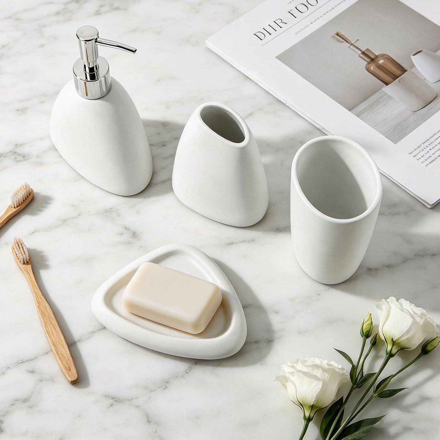 Minimalistisches weißes Badezimmerset auf Marmor: Seifenspender, zwei Becher, Seifenschale mit Seife, Bambus-Zahnbürste und weiße Blumen neben einem Magazin.