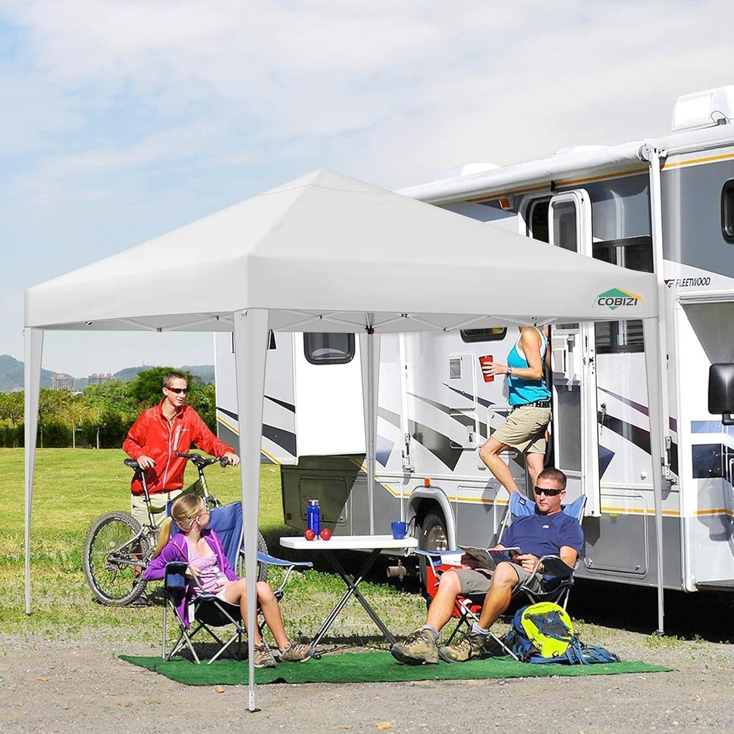 Menschen, die unter einem weißen Baldachin neben einem Wohnmobil entspannen, mit Campingstühlen, einem Fahrrad und Campingausrüstung auf einem Straßen-Campingplatz.