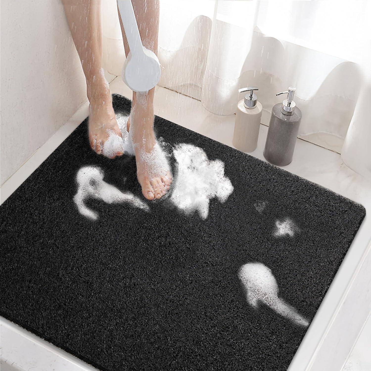 Person spült Seife von den Füßen unter der Dusche auf einer schwarzen Badmatte ab, mit Shampoo- und Seifenspendern in der Nähe.