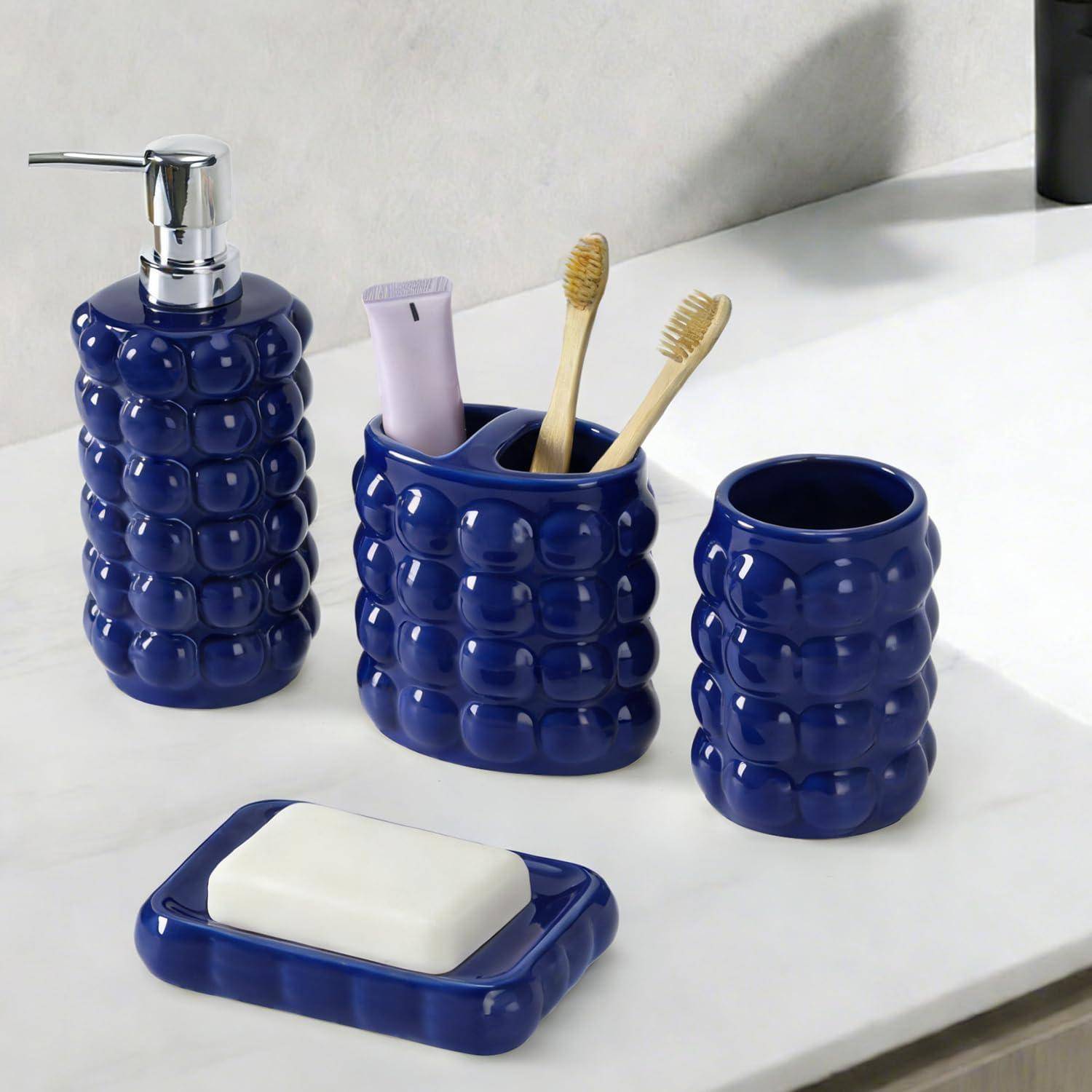 Blaues Keramik-Badezimmerset mit Seifenspender, Zahnbürstenhalter mit zwei Zahnbürsten und einer Tube, Becher und Seifenschale auf einer weißen Arbeitsplatte.