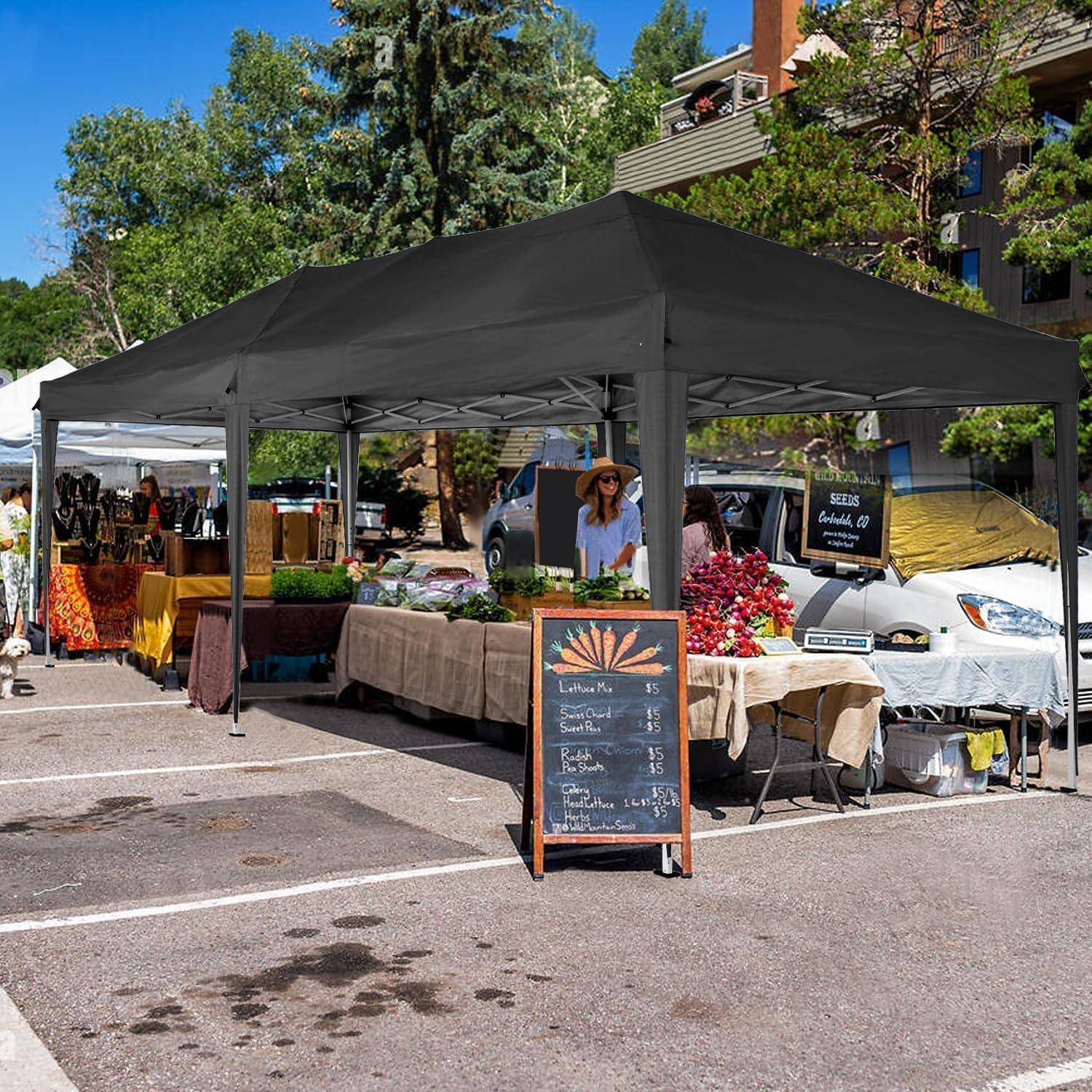 Marktstand auf dem Freiluftbauernmarkt unter schwarzem Zeltdach mit Obst und Gemüse sowie handgefertigten Waren, Verkäufer hinter den Tischen, Kreidetafel-Preisschilder, geparkte Autos in der Nähe.
