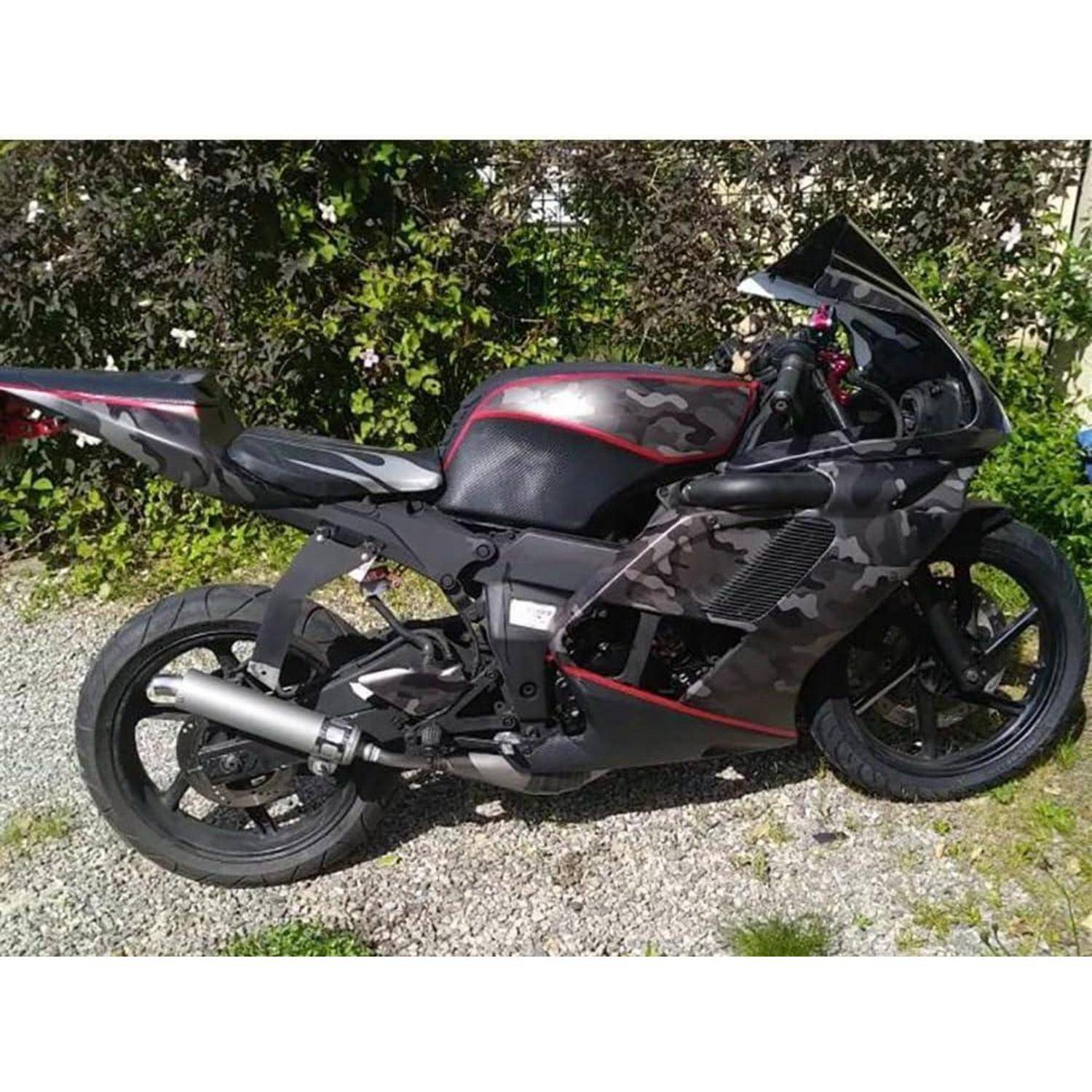 Schwarzes und Tarnmuster-Sportmotorrad, das tagsüber auf Kies neben einer Hecke geparkt ist.