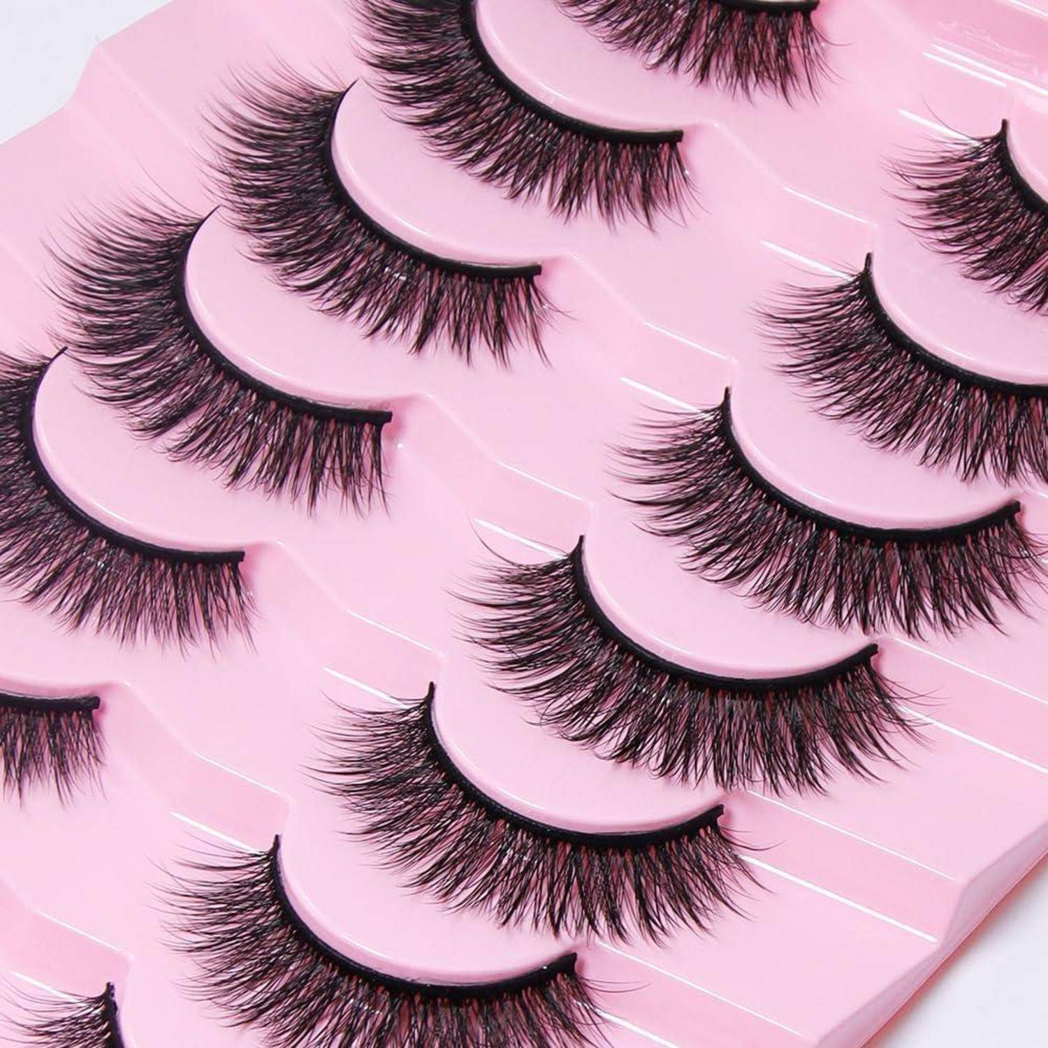 Mehrere Paar künstliche Wimpern, die auf rosa gekrümmten Tabletts in einer ordentlich arrangierten Produktnahaufnahme angezeigt werden.