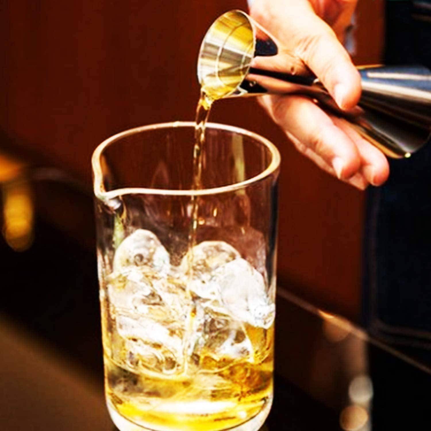 Hand gießt Whiskey aus einem Messbecher in ein Glas mit Eis in einer Bar-Umgebung.