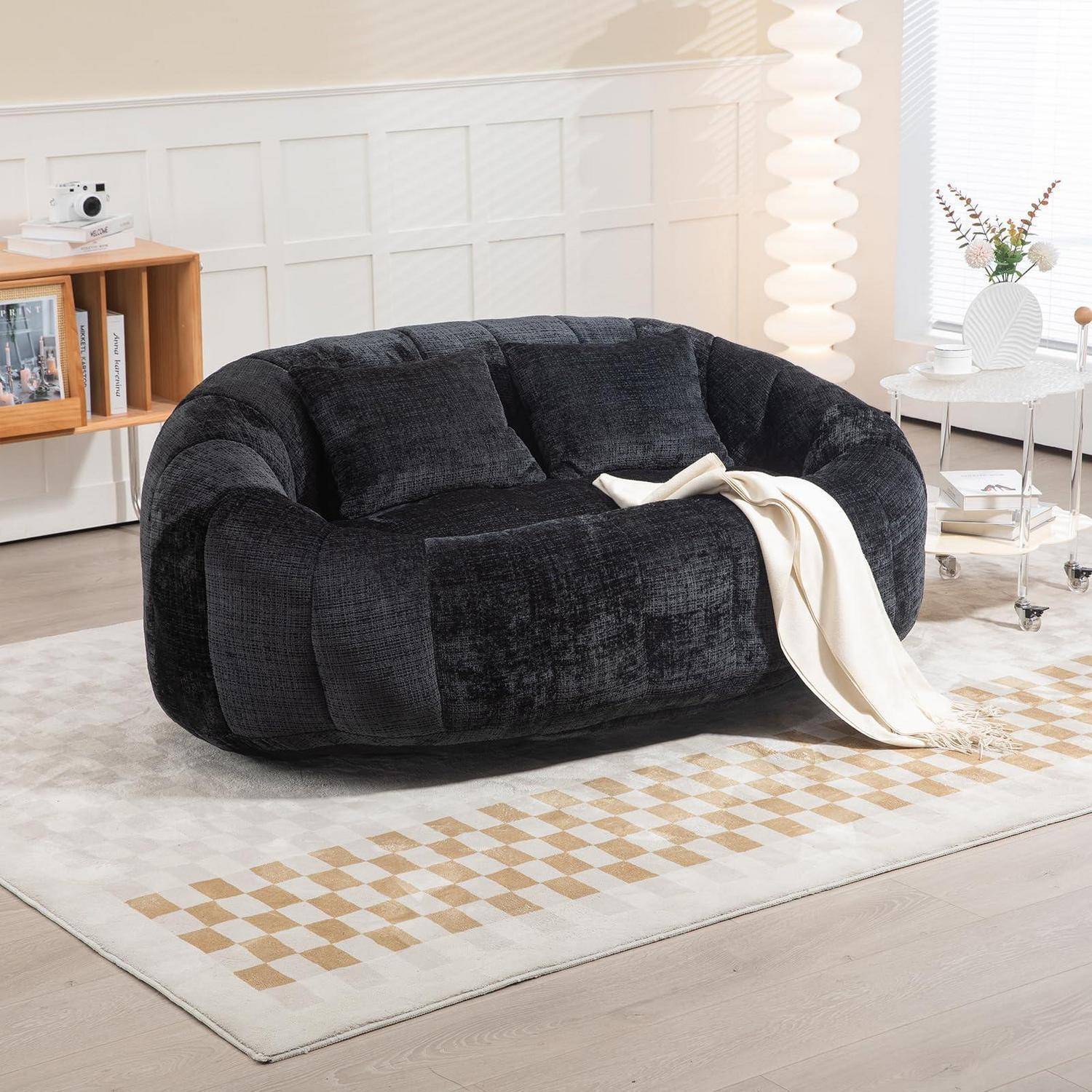 Schwarzes gerundetes Loveseat-Sofa mit cremefarbenener Wurfdecke in einem hellen, modernen Wohnzimmer mit Teppich, Beistelltischen und Dekoration.
