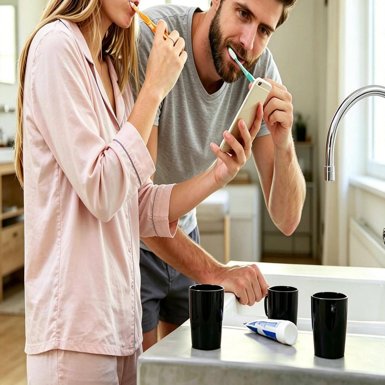 Ein Paar in Schlafanzügen putzt sich gemeinsam die Zähne im Badezimmer, während es auf ein Smartphone auf dem Waschbecken schaut.