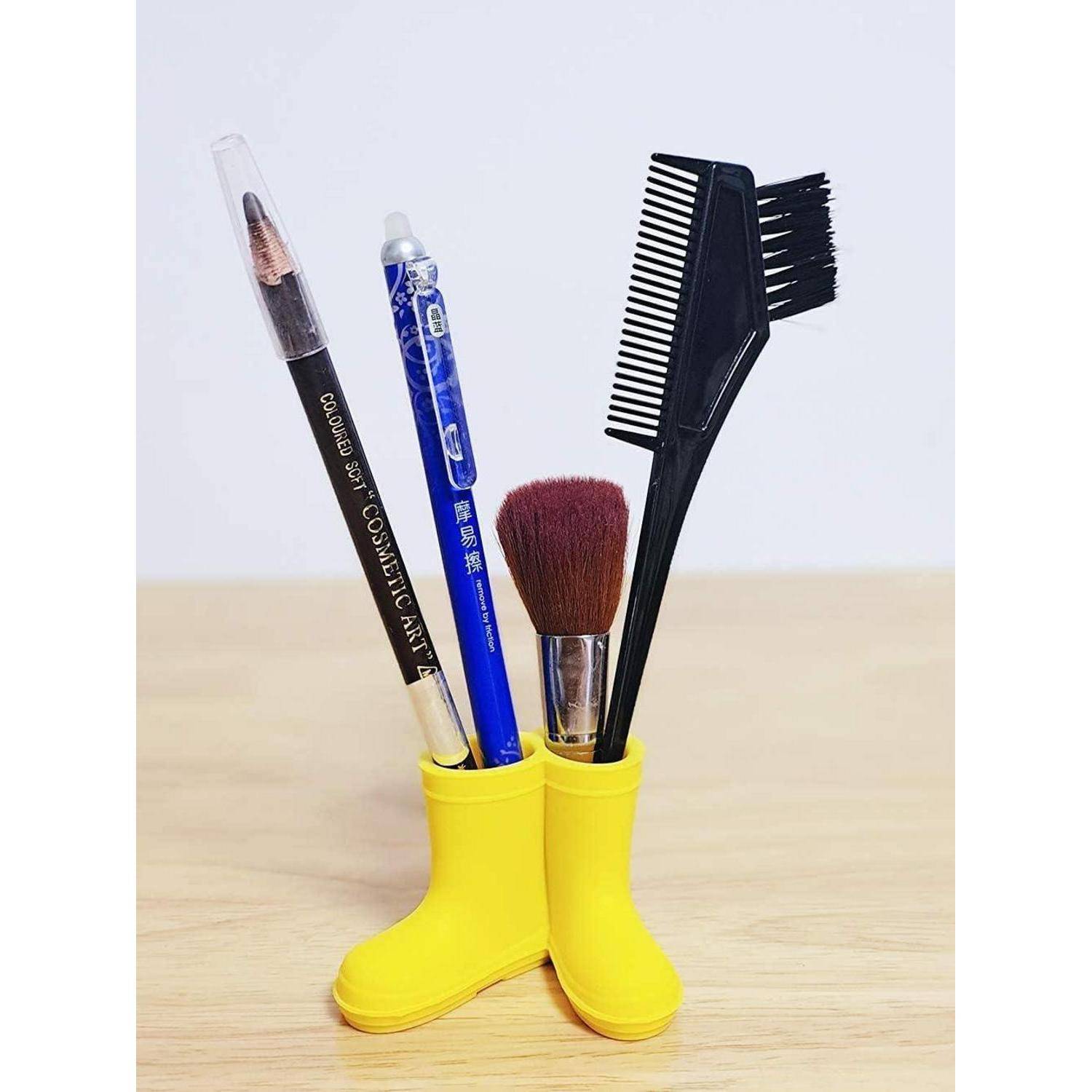 Gelber stiefelförmiger Stifthalter mit einem Makeup-Pinsel, einem Eyeliner-Stift, einem blauen Stift und einem schwarzen Kamm auf einem Holztisch.