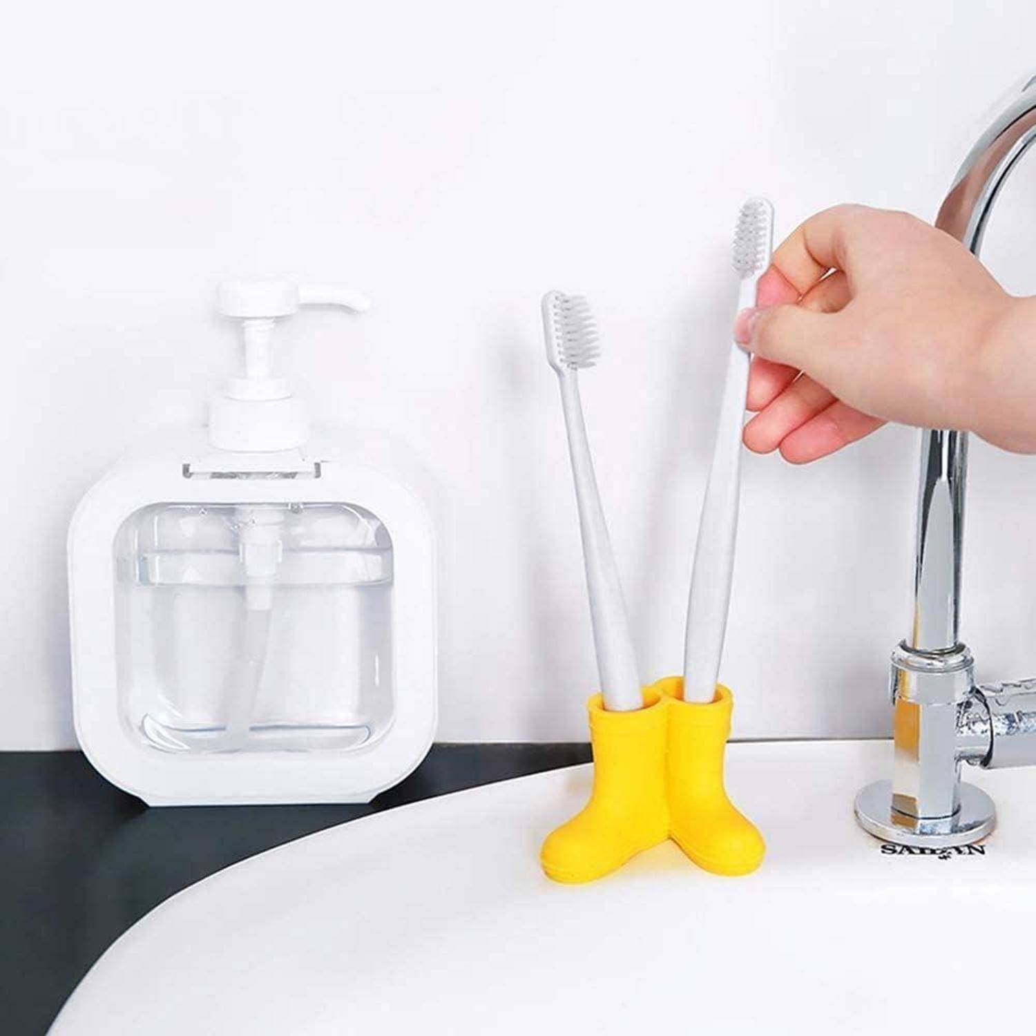 Hand, die eine Zahnbürste in einen gelben, stiefelförmigen Halter neben einem Waschbecken legt, mit einem wandmontierten Seifenspender in der Nähe.