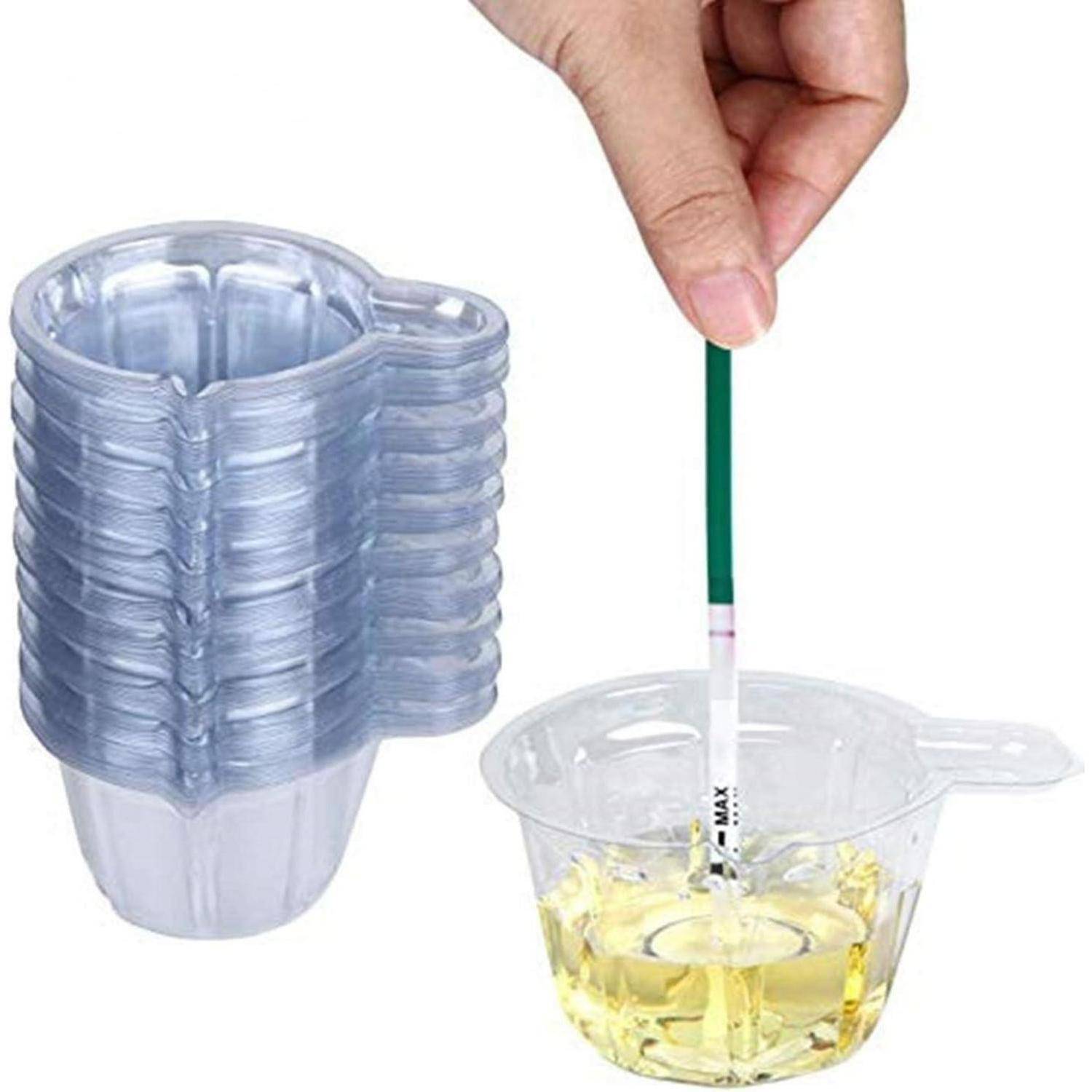 Eine Hand hält einen Teststreifen in einem durchsichtigen Kunststoffbecher mit gelber Flüssigkeit neben einem Stapel verschachtelter Becher, was auf ein Urin- oder Flüssigkeitstestkit hindeutet.