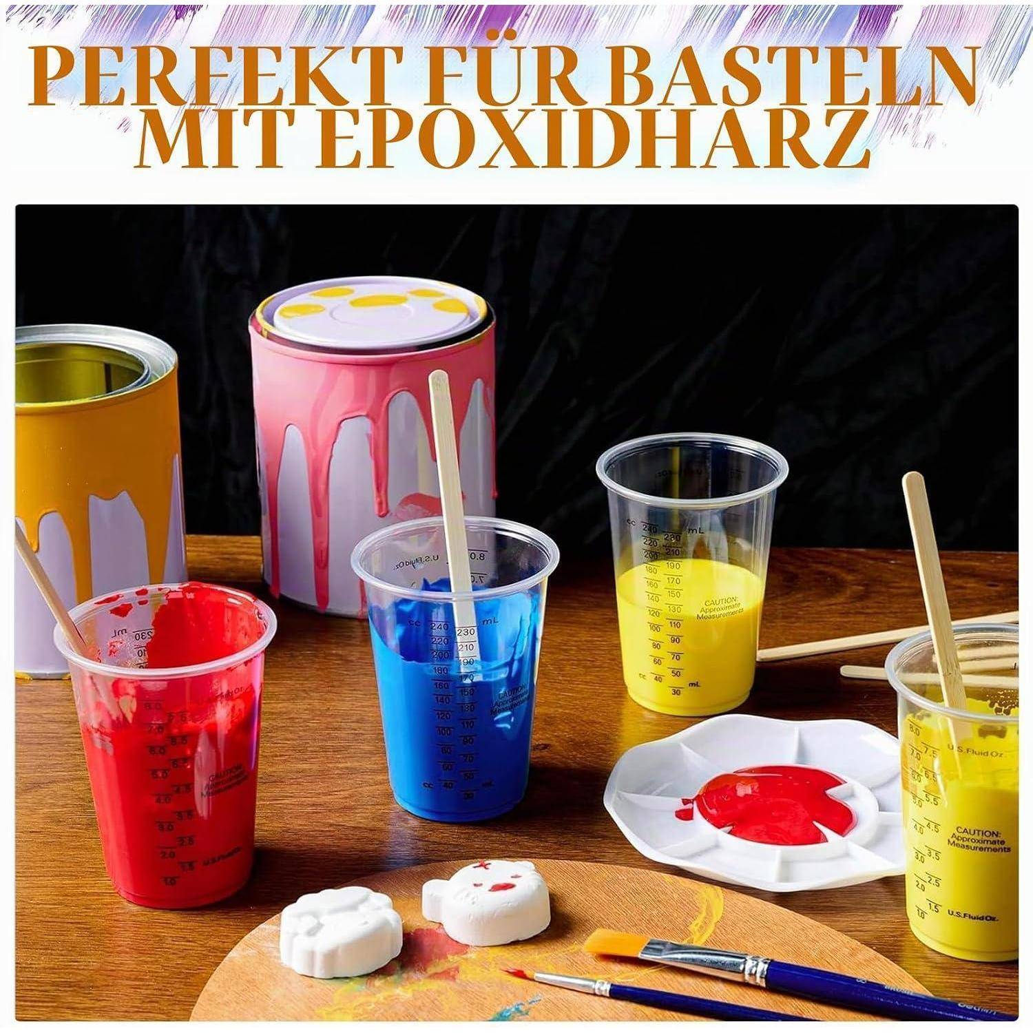 Handwerk-Setup für Epoxidharz: farbiges Harz in Messbechern neben Farbdosen, Formen, Pinseln und einer Palette auf einem Holztisch.